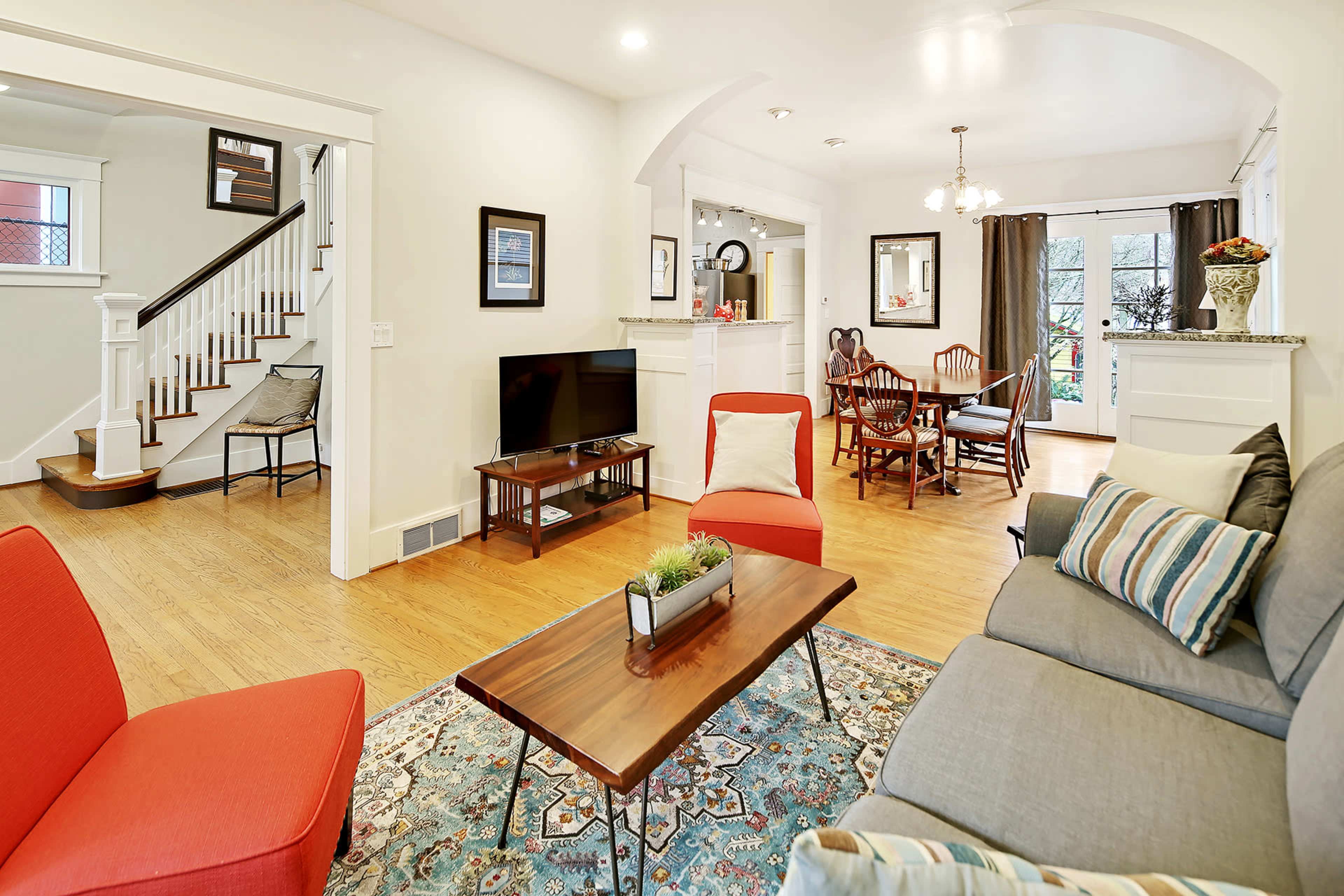 A living room with a gray sofa, red accent chairs, a coffee table, and a connected dining area featuring a round table with chairs and large windows.