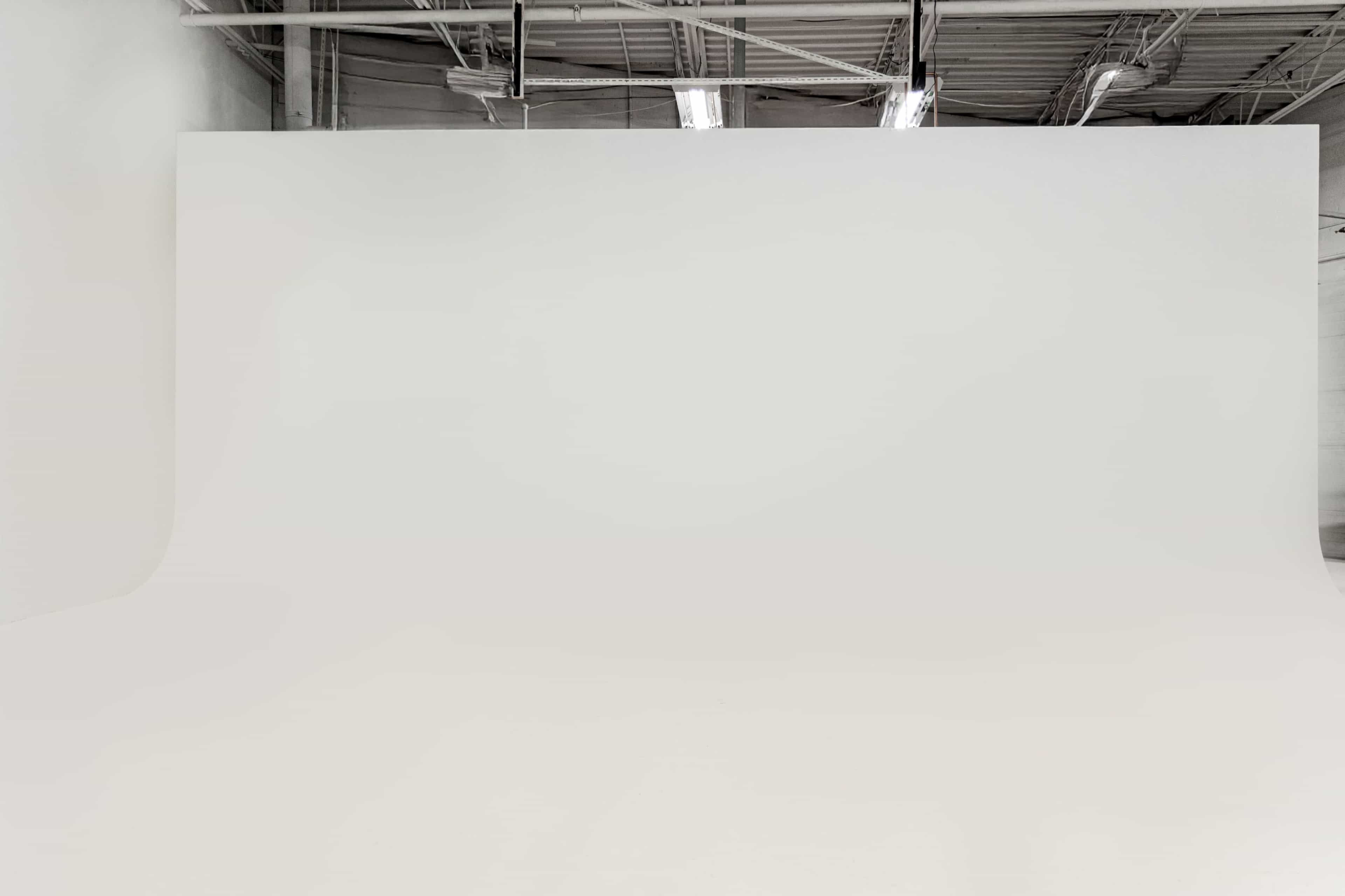 The image shows a spacious, empty room with a seamless white backdrop and a smooth floor.
