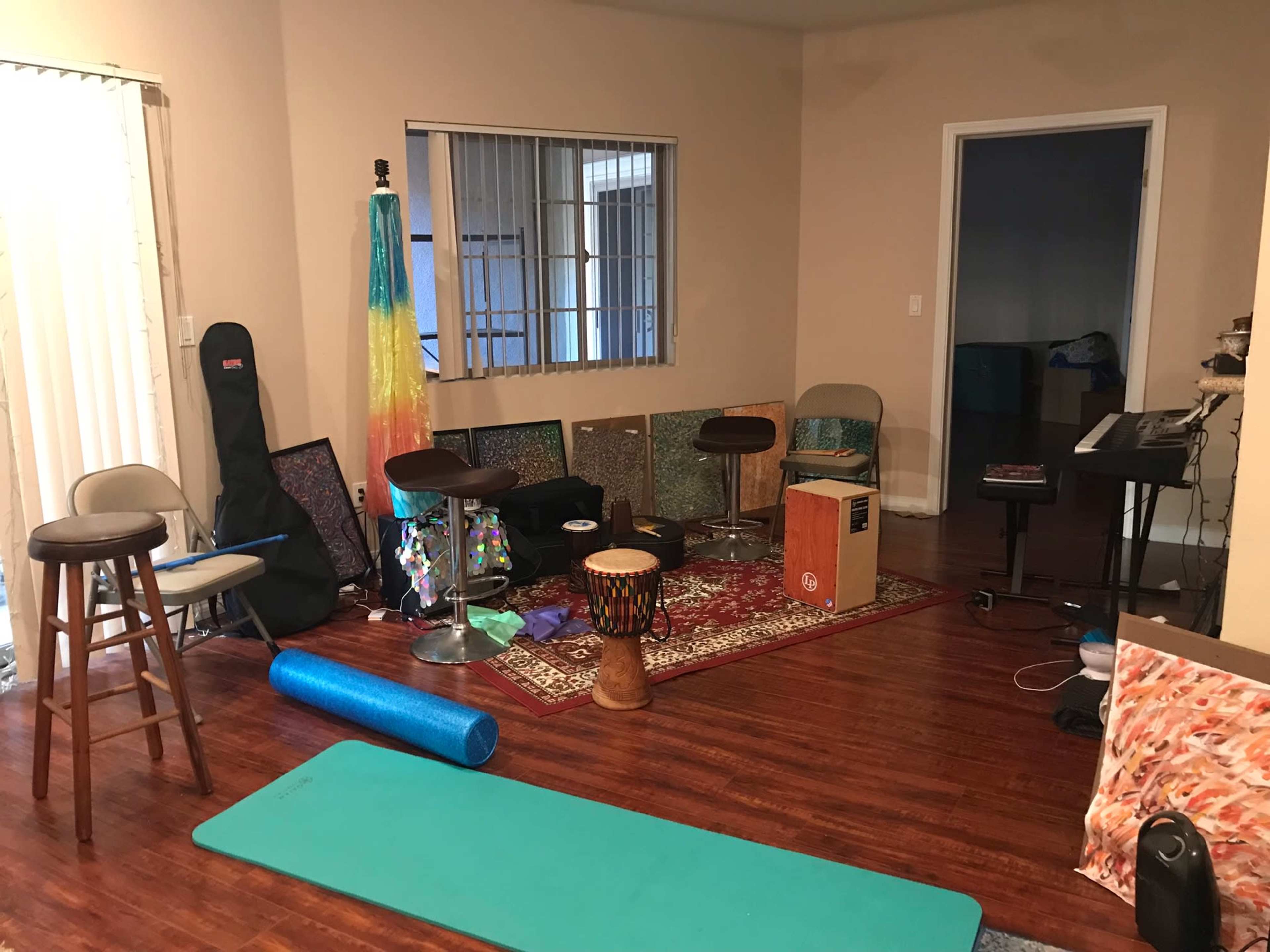 A room containing various musical instruments, exercise equipment, and furniture set against a backdrop of wooden flooring and light-colored walls.
