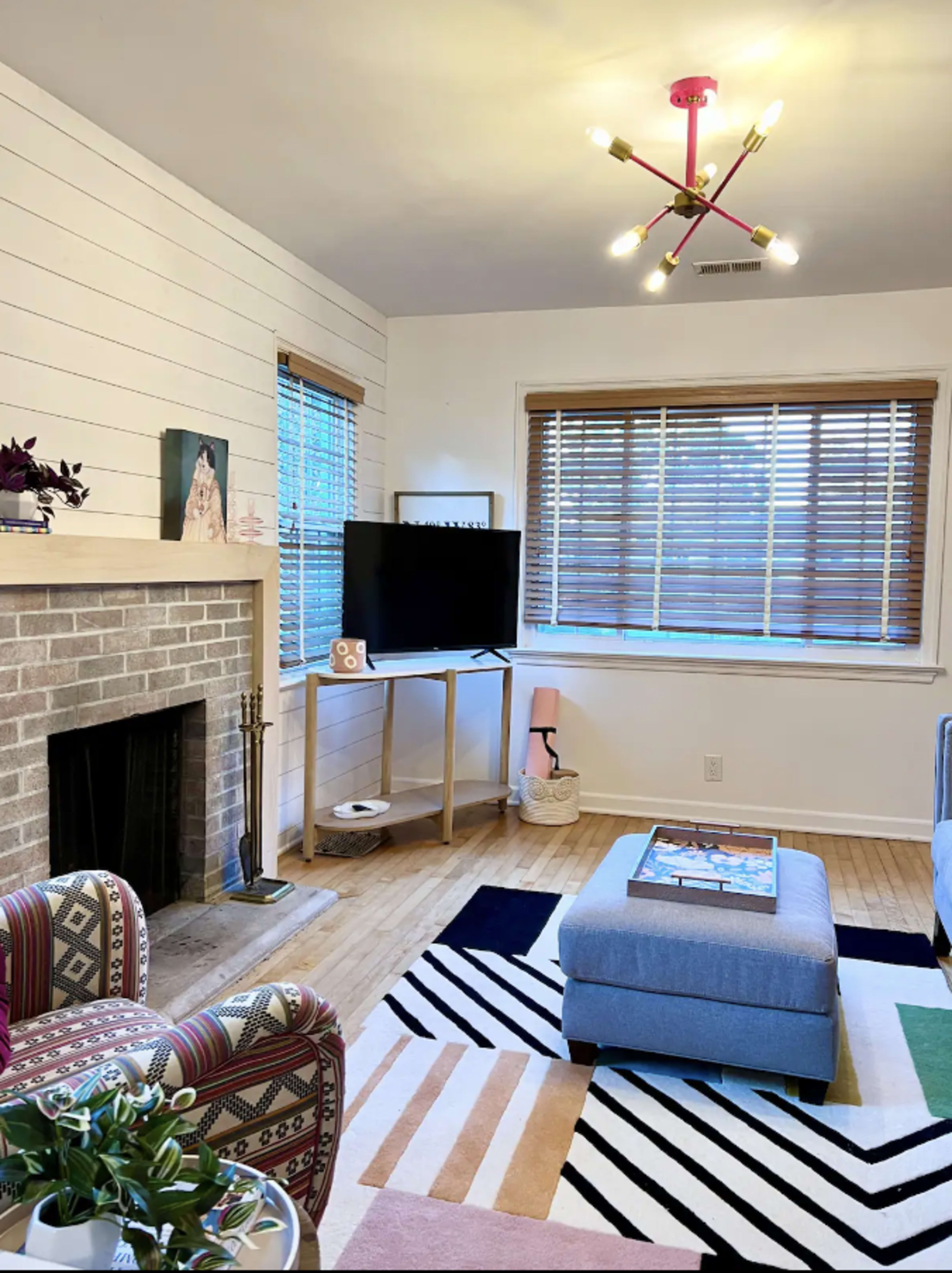 A living room with a brick fireplace, a television on a stand, a colorful rug, and modern furniture.