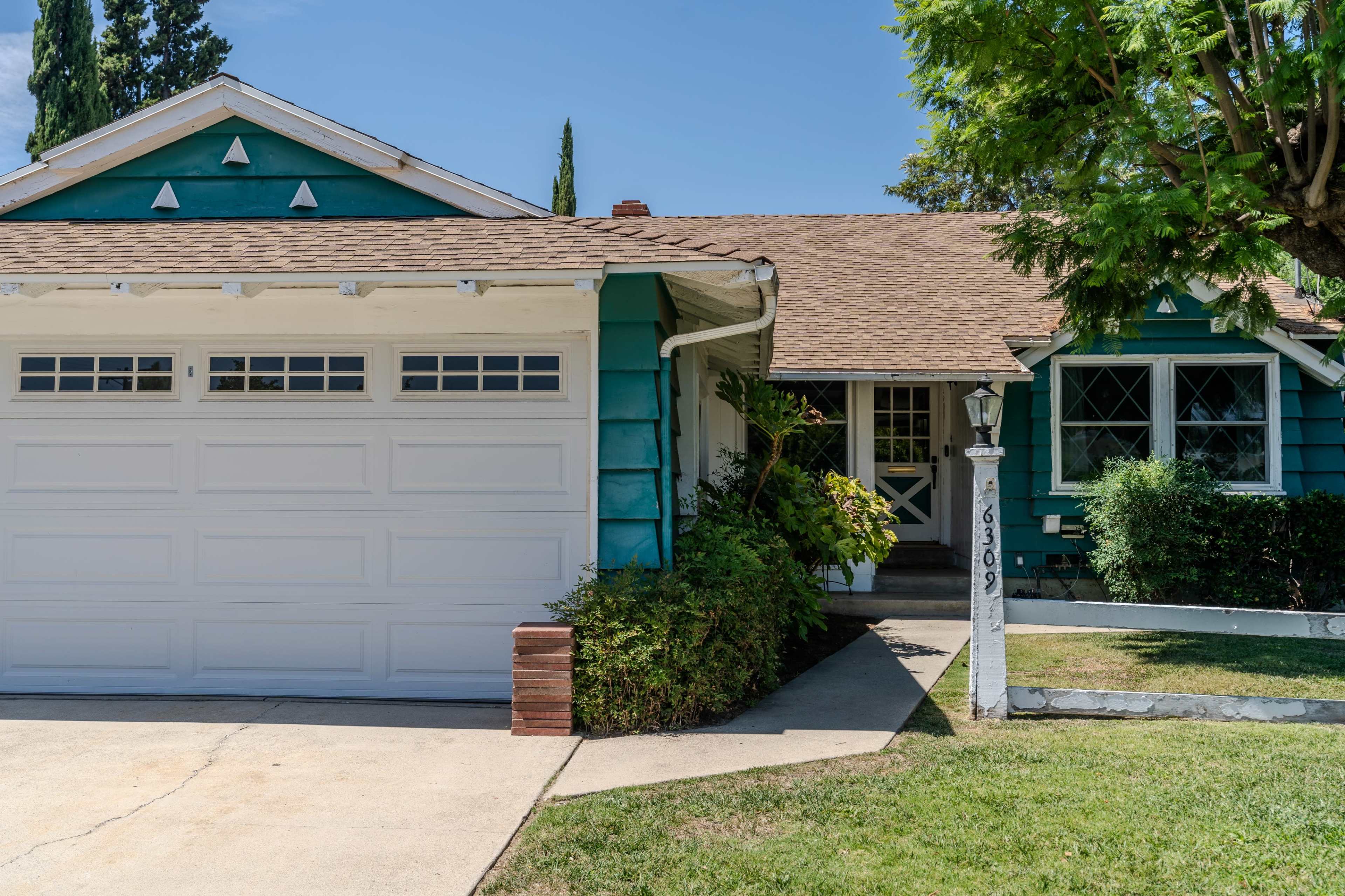 A teal house with a brown shingled roof features a garage and a well-maintained front yard.