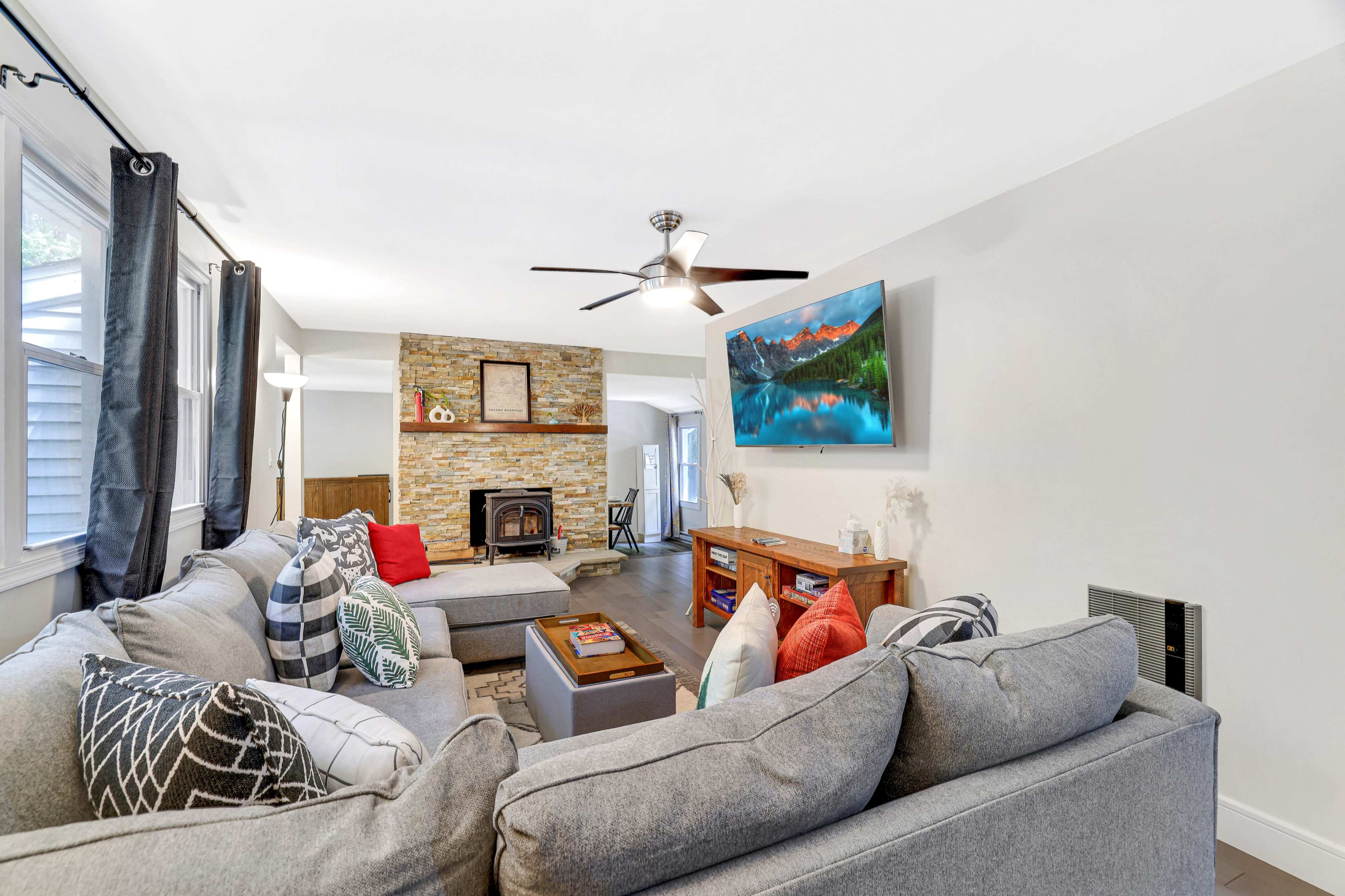 A living room featuring gray sectional sofas, a stone fireplace, and a mounted television above a wooden entertainment unit.