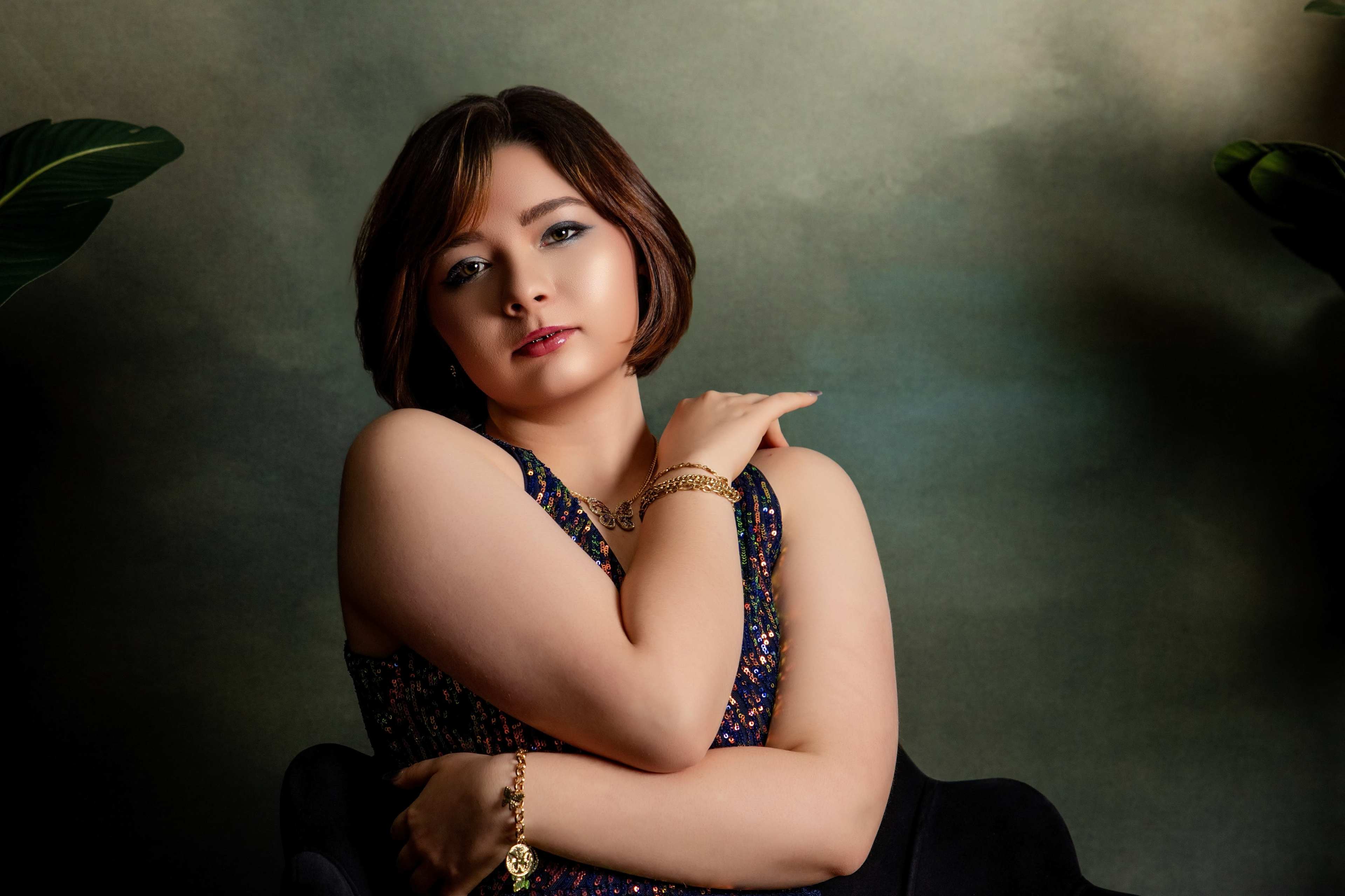 A young woman poses elegantly in a sparkly dress against a soft, greenish background.