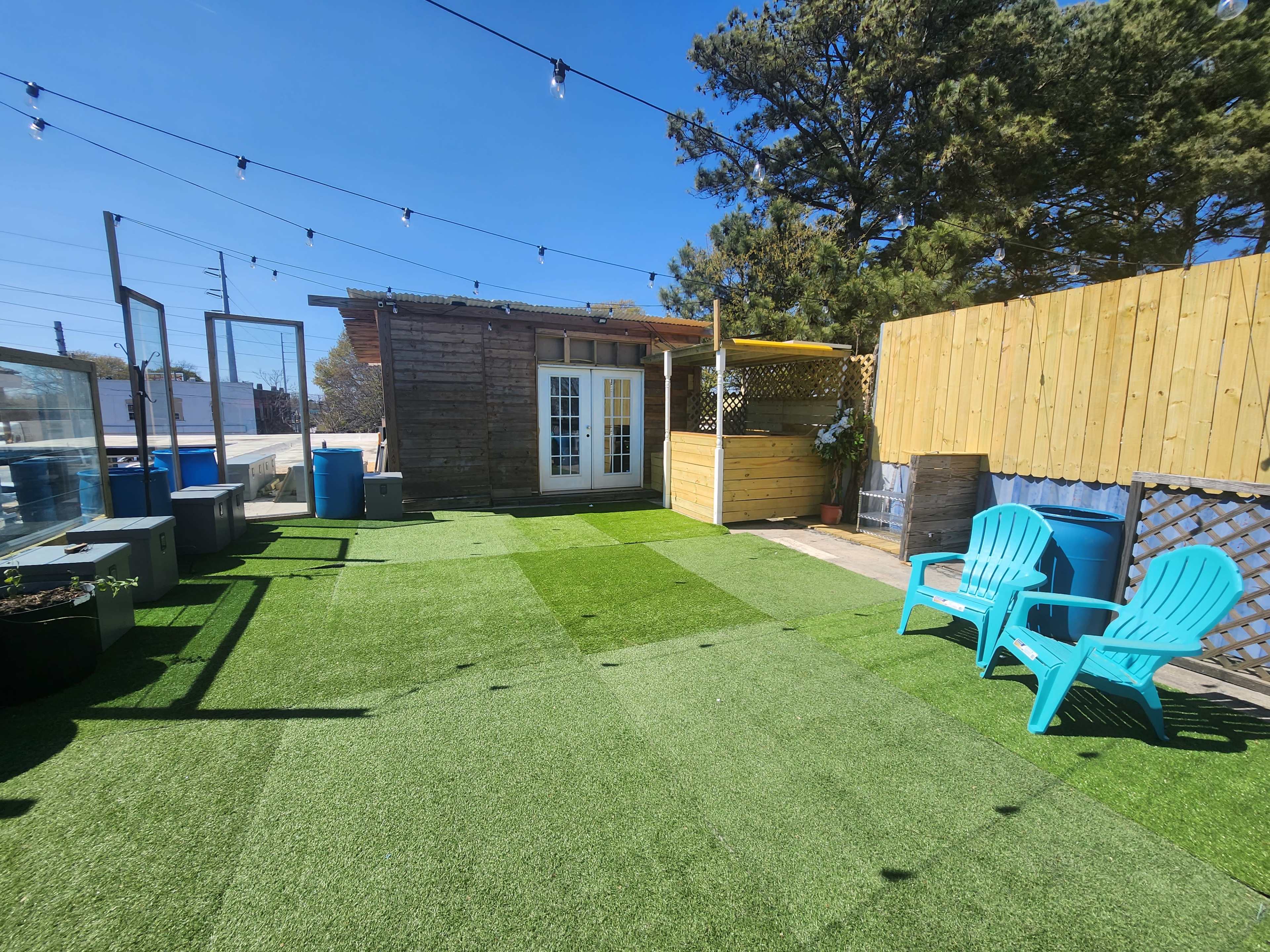 A well-maintained rooftop space featuring artificial grass, two turquoise chairs, and a wooden structure with a door and windows.