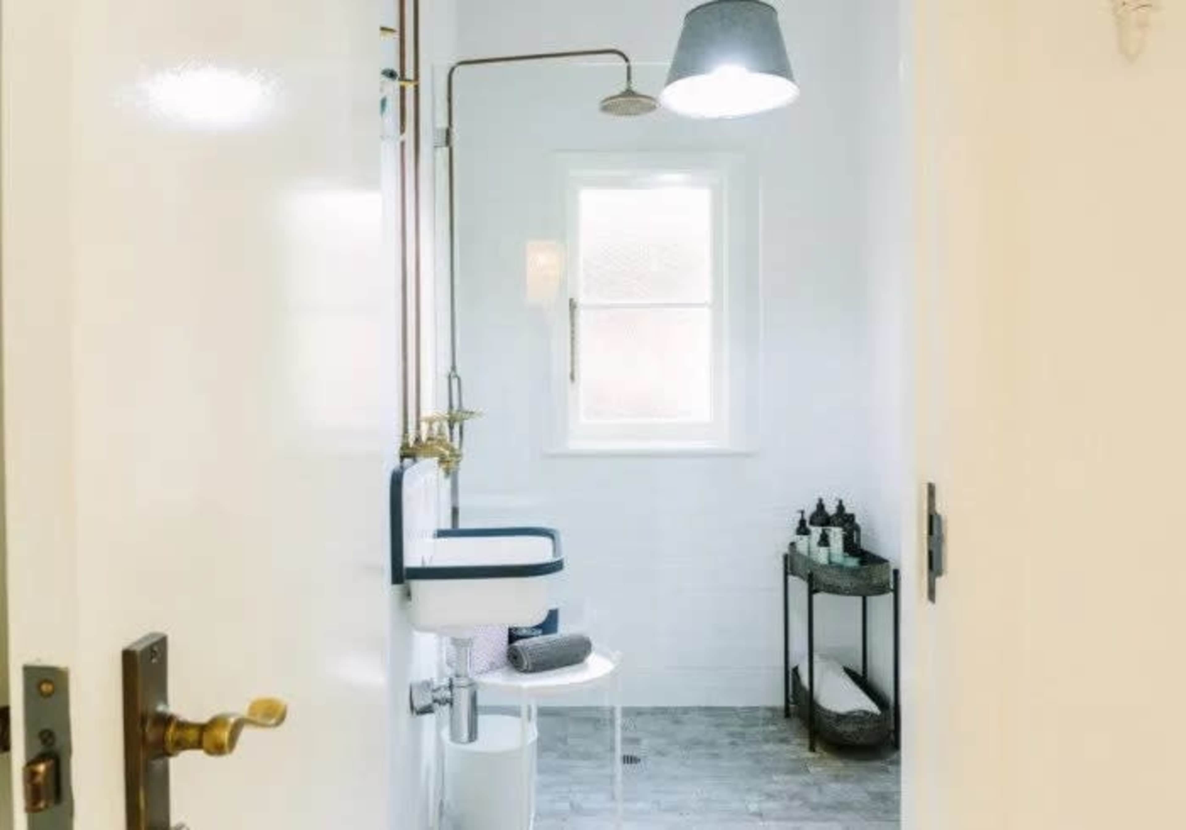 A clean, minimalist bathroom with a shower, a modern toilet, and a small storage cart containing toiletries.