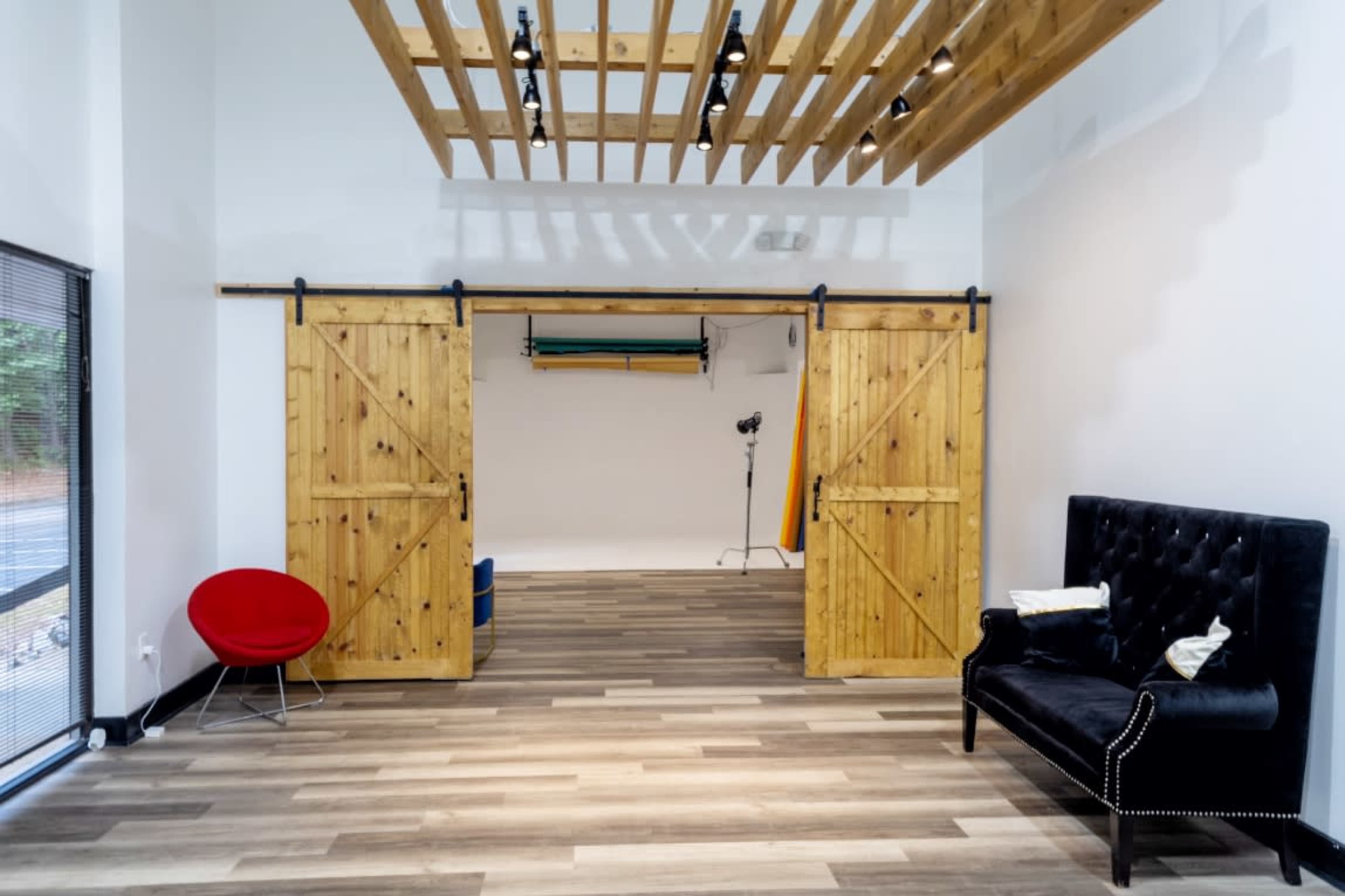The image shows a spacious interior with wooden sliding doors, a black velvet sofa, and studio lighting equipment in the background.