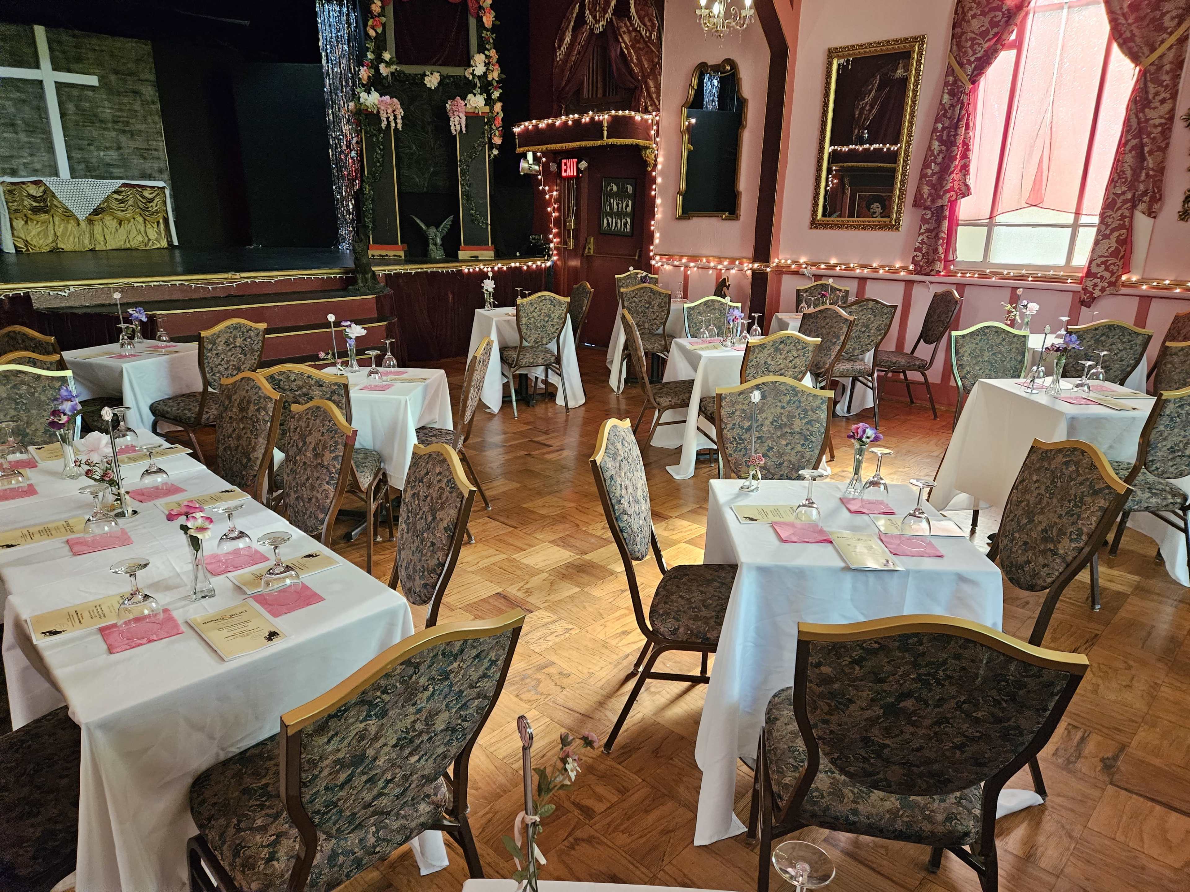 A banquet hall set with several dining tables, each adorned with white tablecloths and floral centerpieces, arranged for an event.