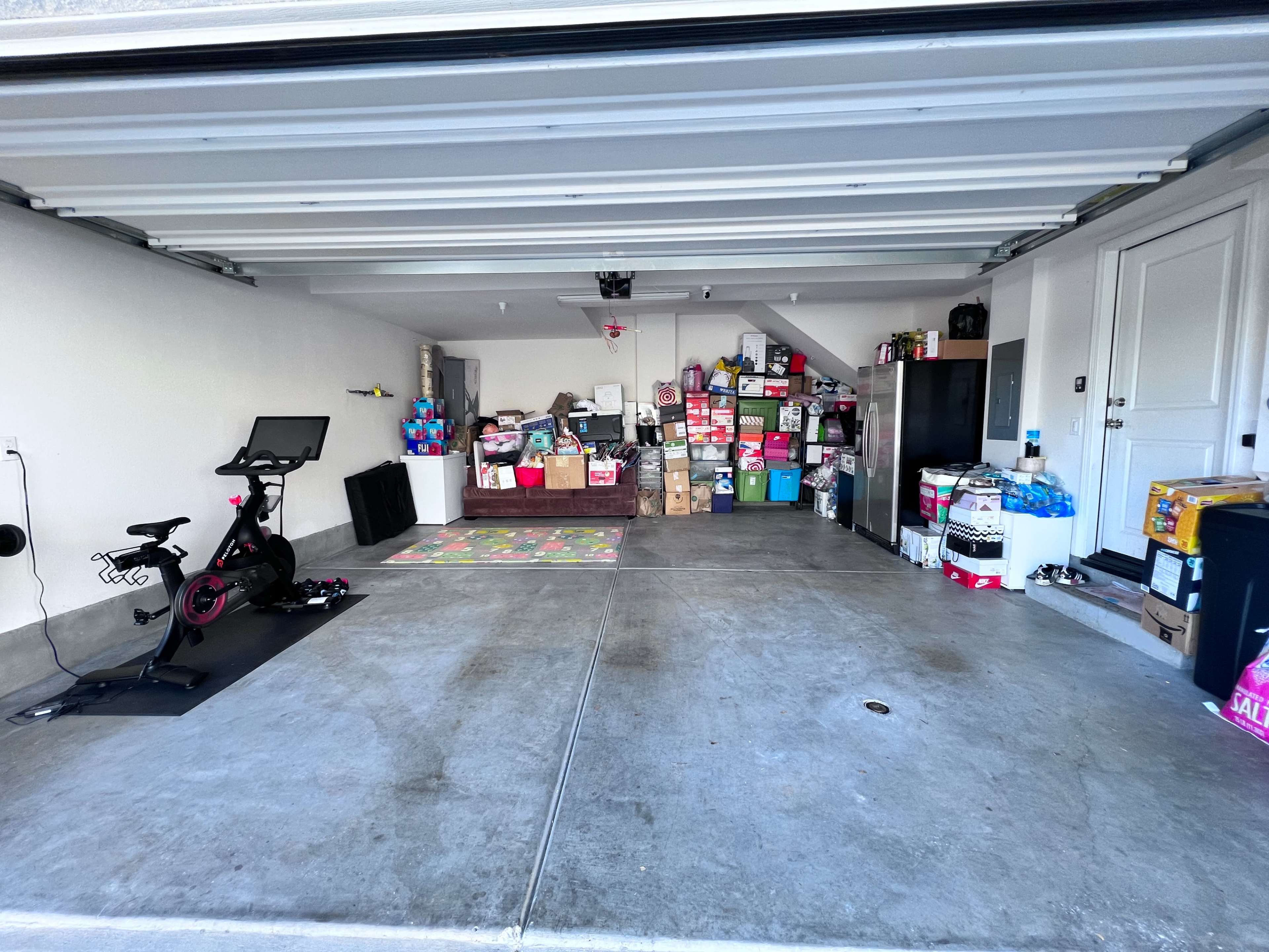 A garage with a mix of stacked boxes, a stationary bike, and shelves filled with various items.