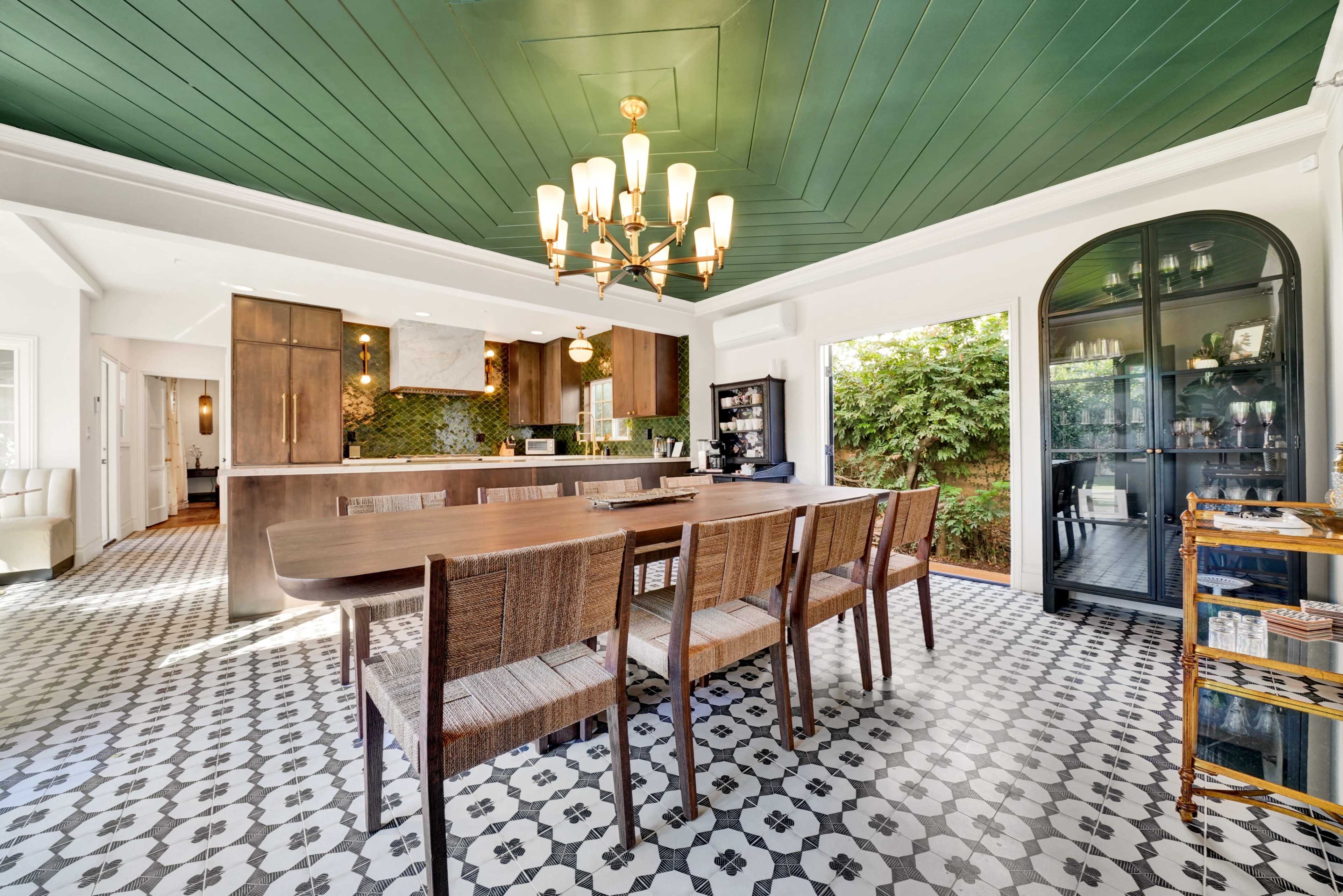 The image shows a modern kitchen and dining area with a long wooden table, pendant lighting, and patterned tile flooring.