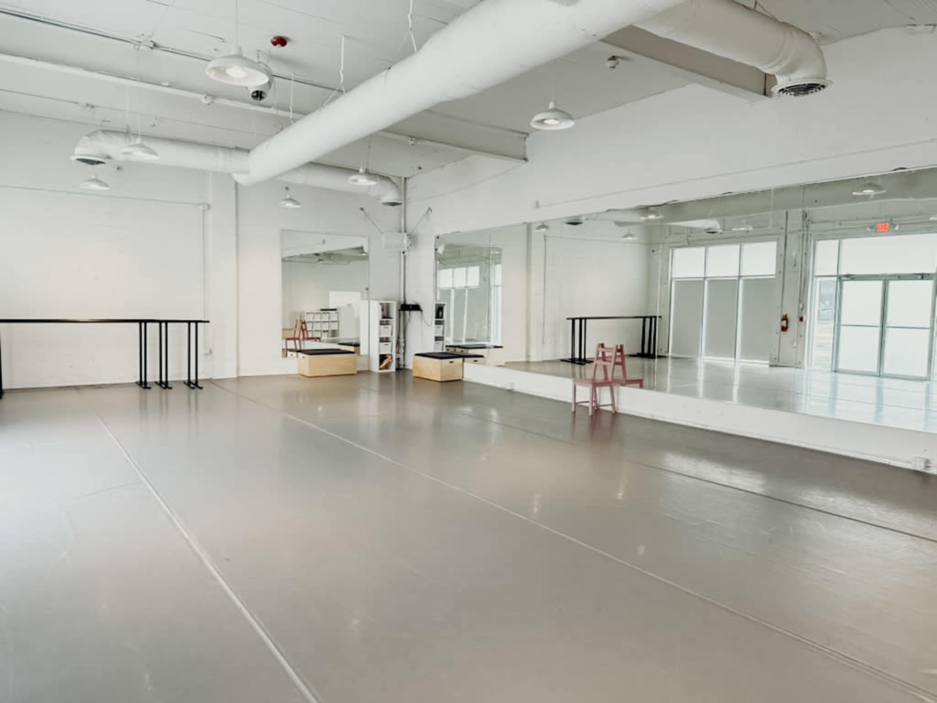 The image shows a spacious, well-lit dance studio with mirrored walls and a gray floor.