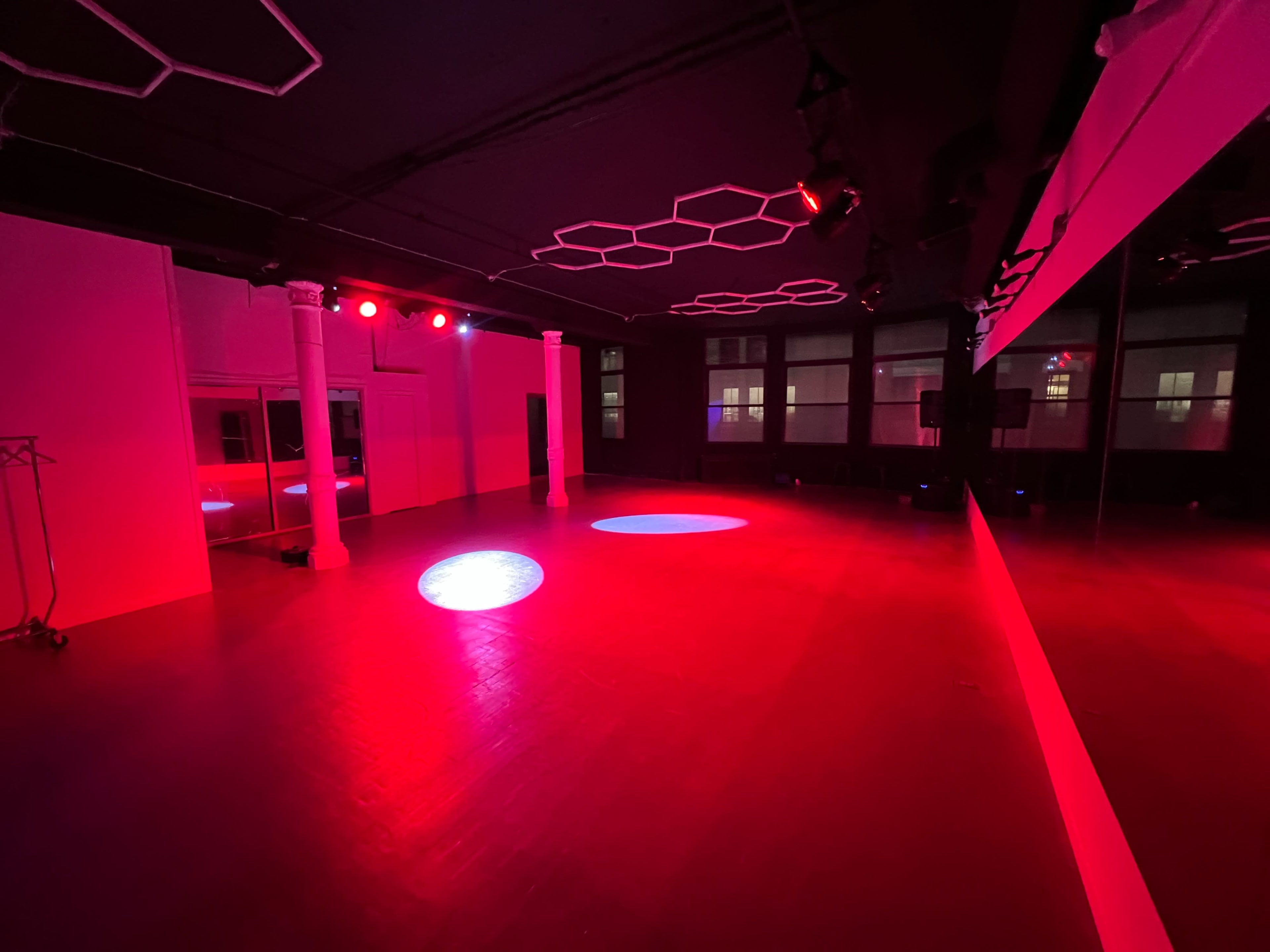 The image shows an empty studio space with a reflective wall, illuminated by red lighting from overhead fixtures.