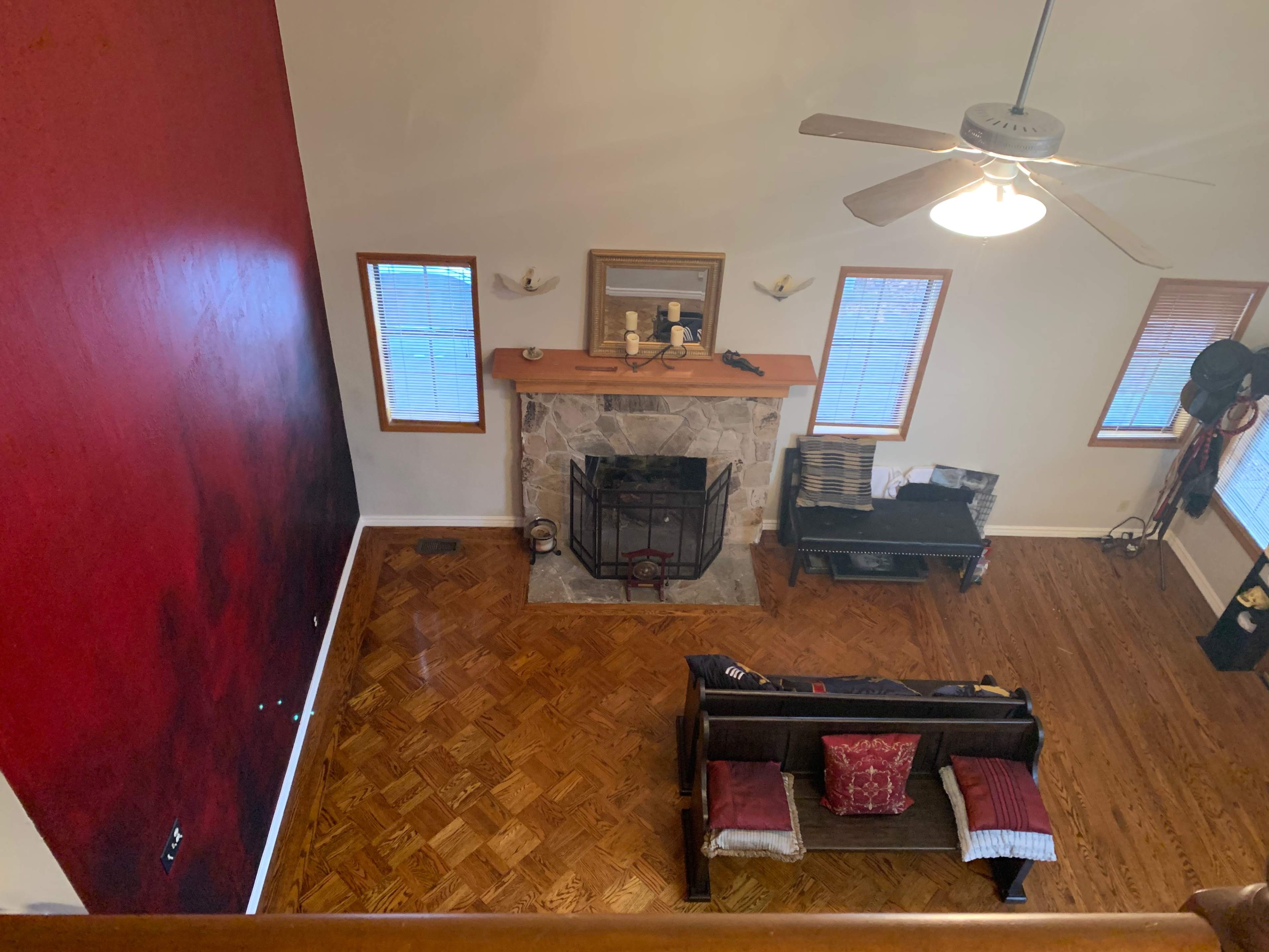 The image shows a spacious living room with a stone fireplace, wooden floor, and a red accent wall.