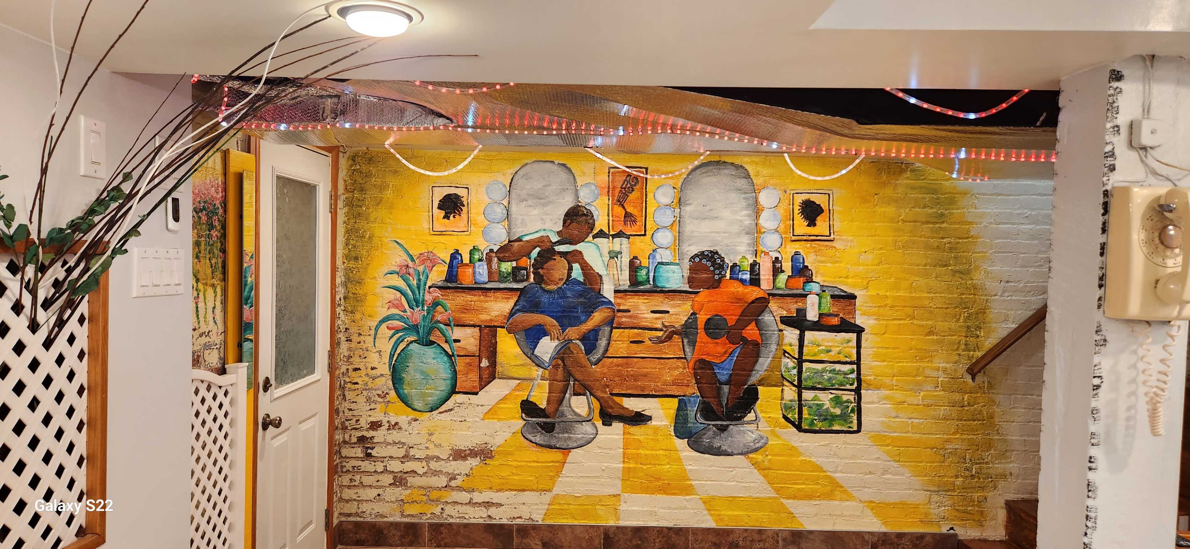 The mural depicts two individuals sitting in salon chairs, surrounded by beauty products and a vibrant interior.