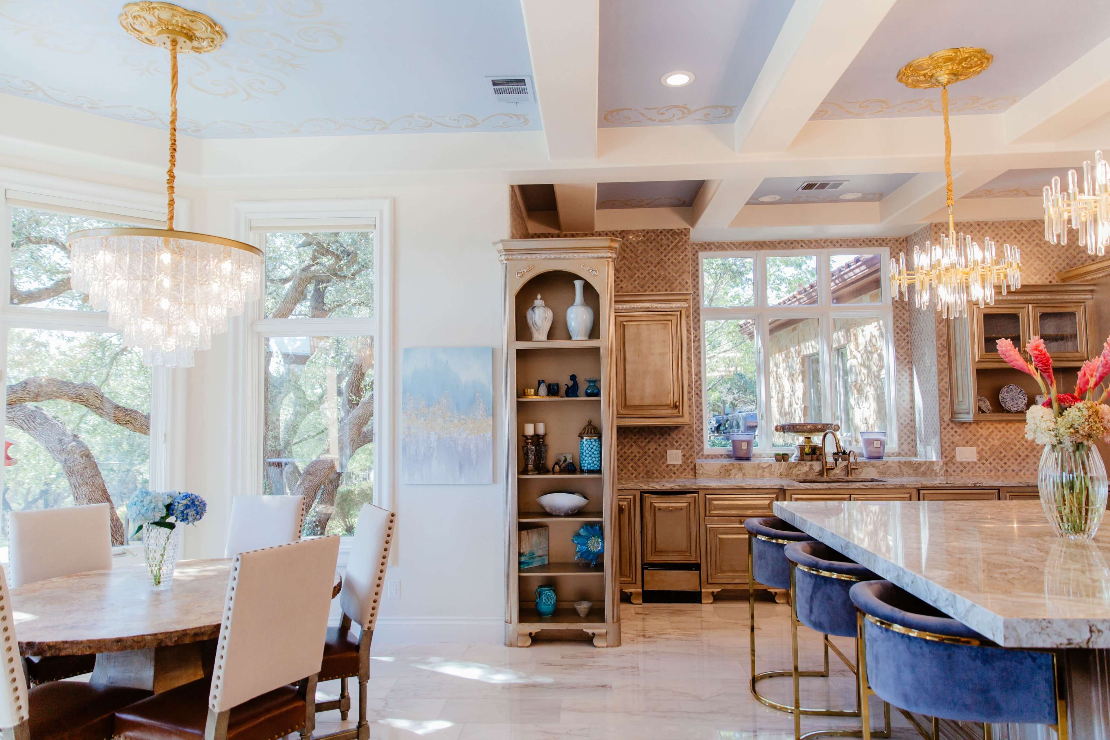 A bright kitchen and dining area featuring a large island with seating, a wooden dining table, and shelves displaying decorative items.