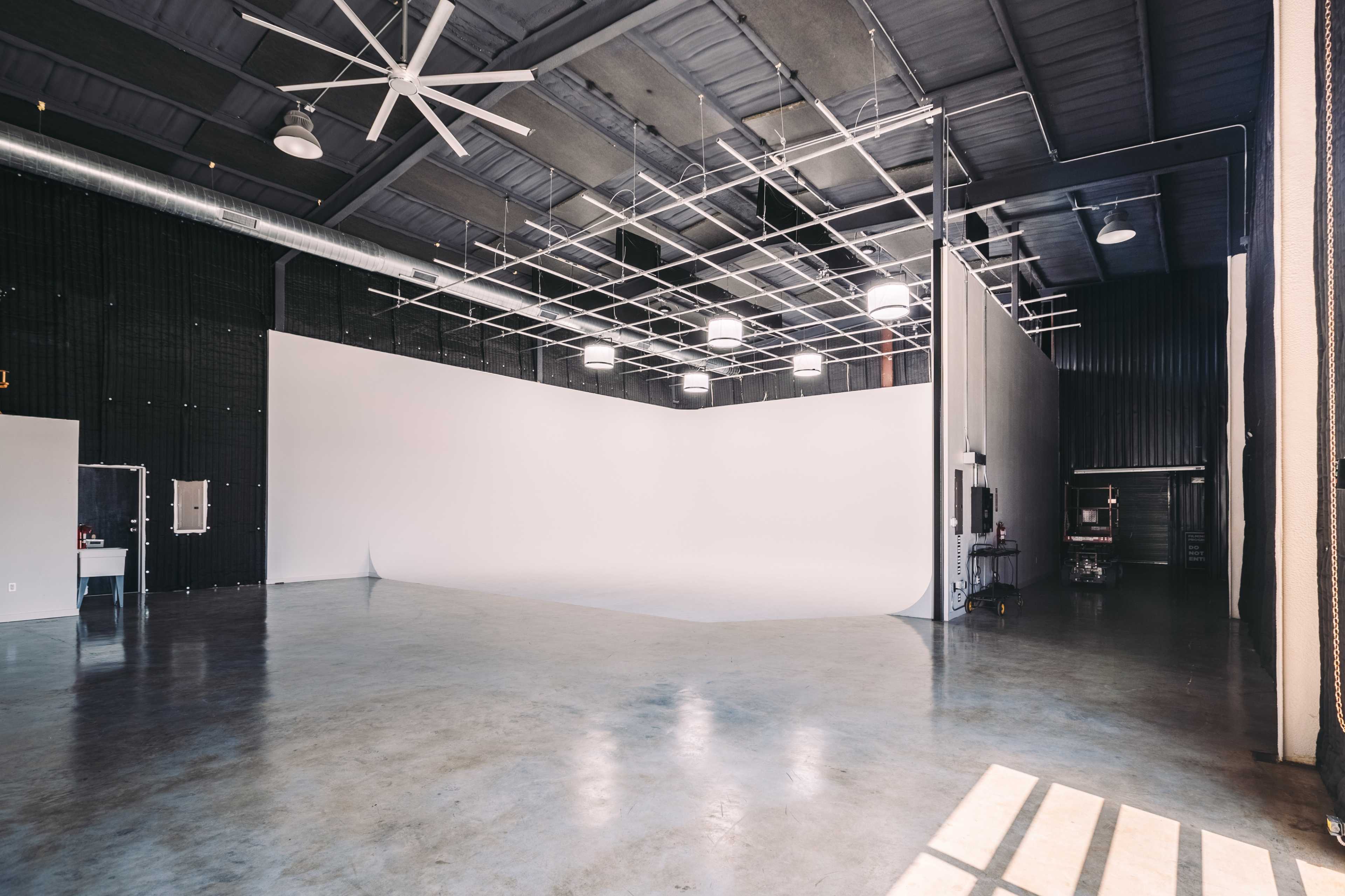 The image shows an empty photo studio with a large, white seamless backdrop and high ceilings.