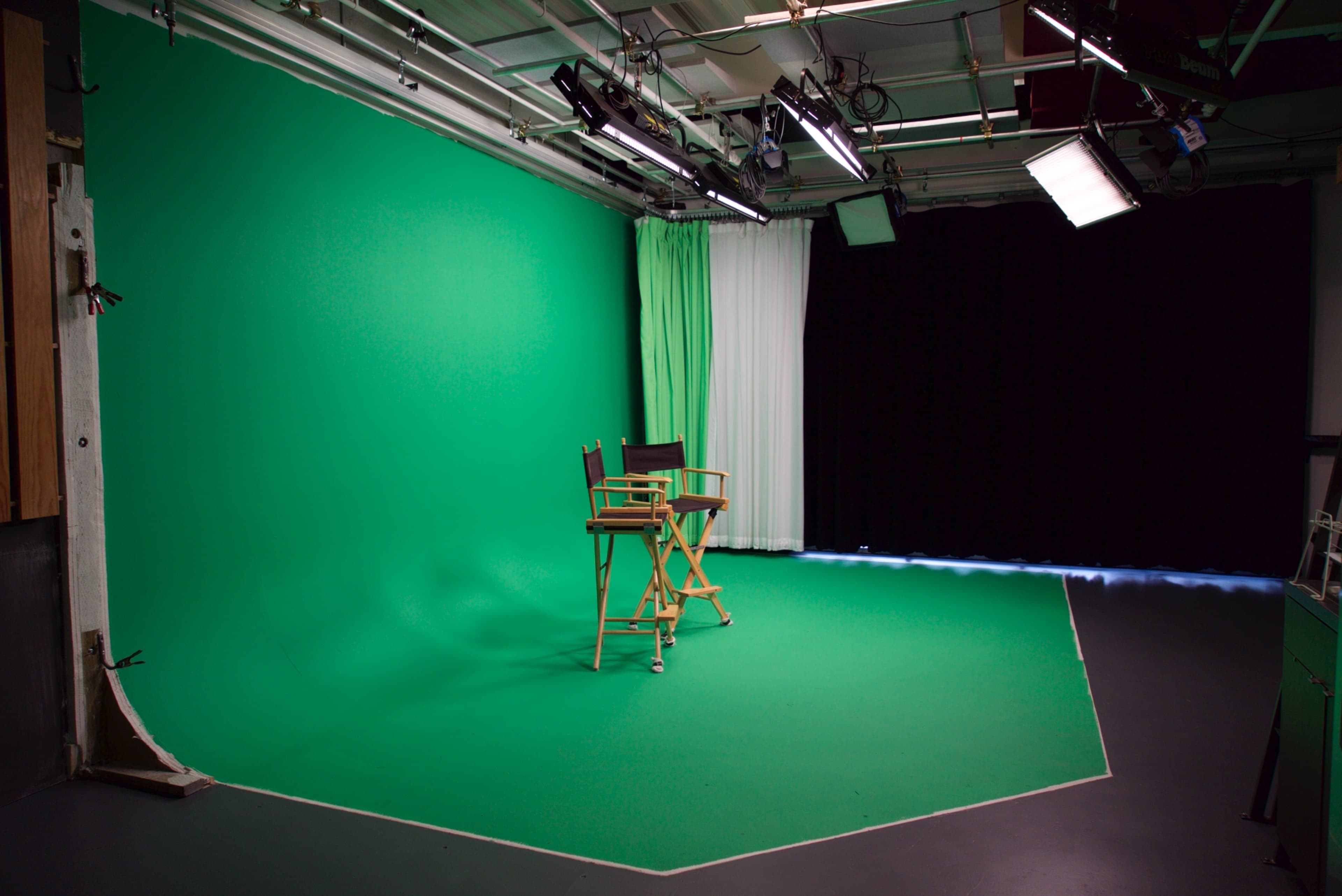 The image shows a studio space with a green screen backdrop and two director's chairs positioned in front of it.
