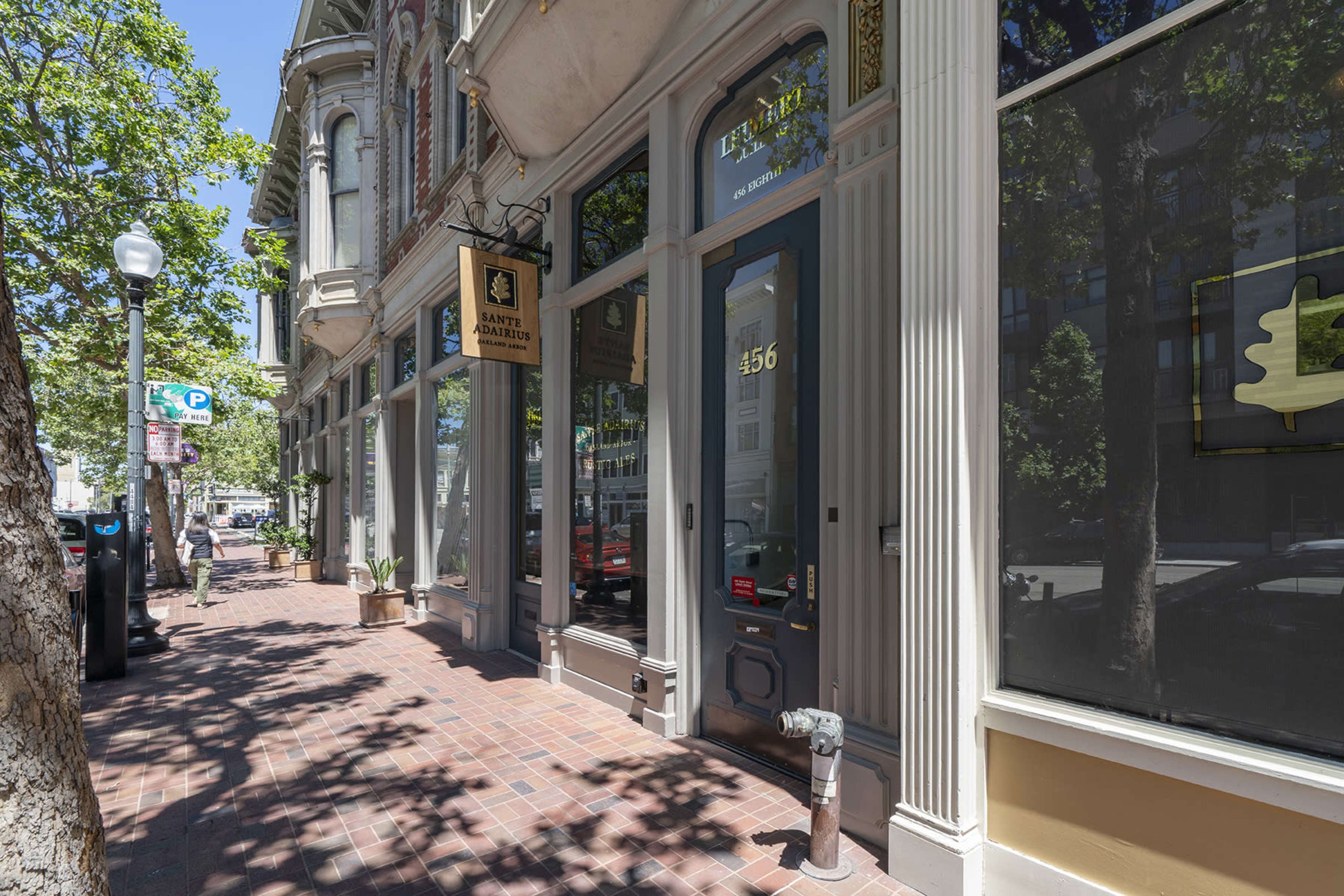 A tree-lined sidewalk in front of a historic building with large windows and a door labeled "456."