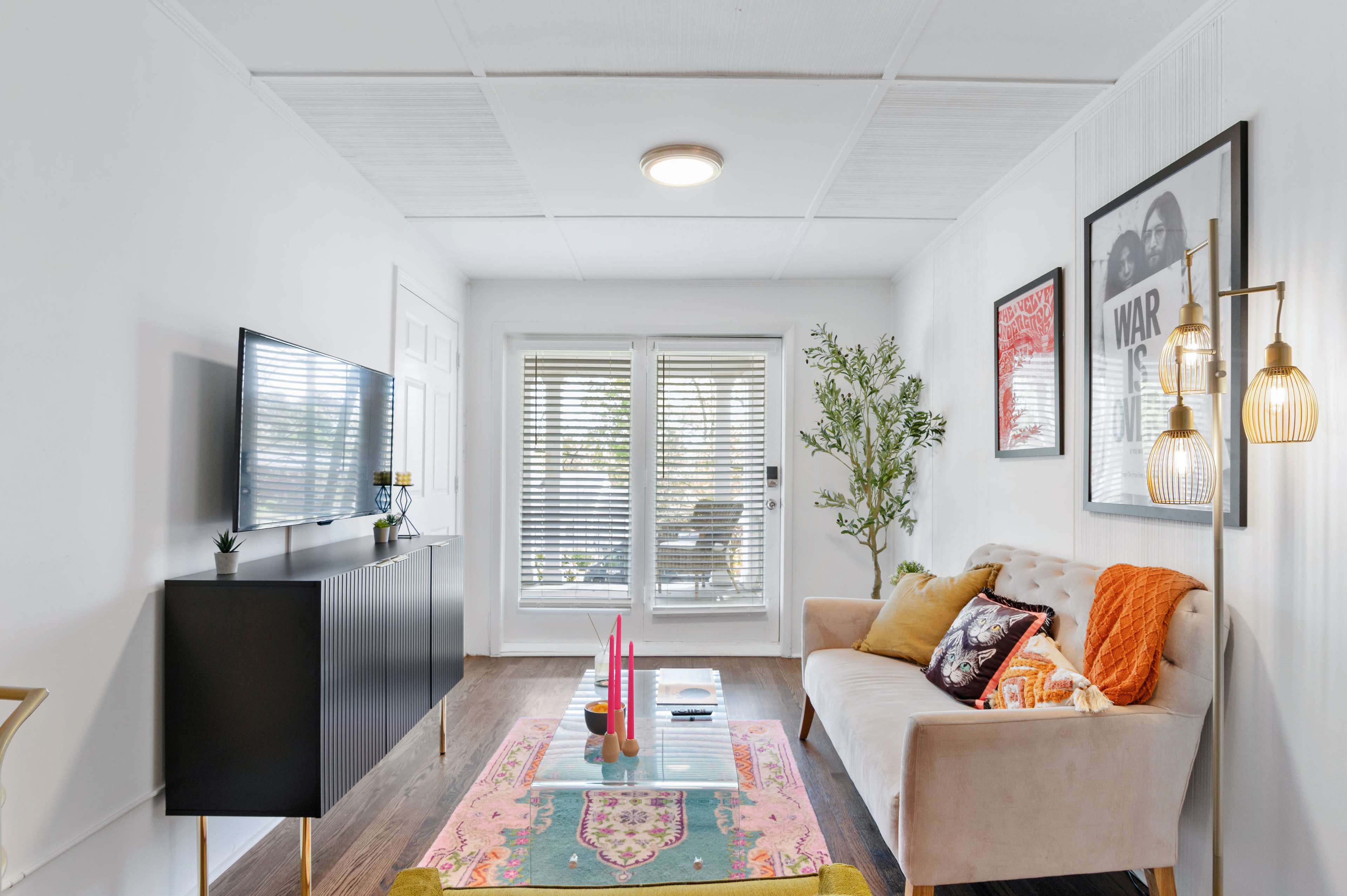 A bright living room featuring a beige sofa, a black television cabinet, a glass coffee table with decorative items, and sliding doors leading to a patio.