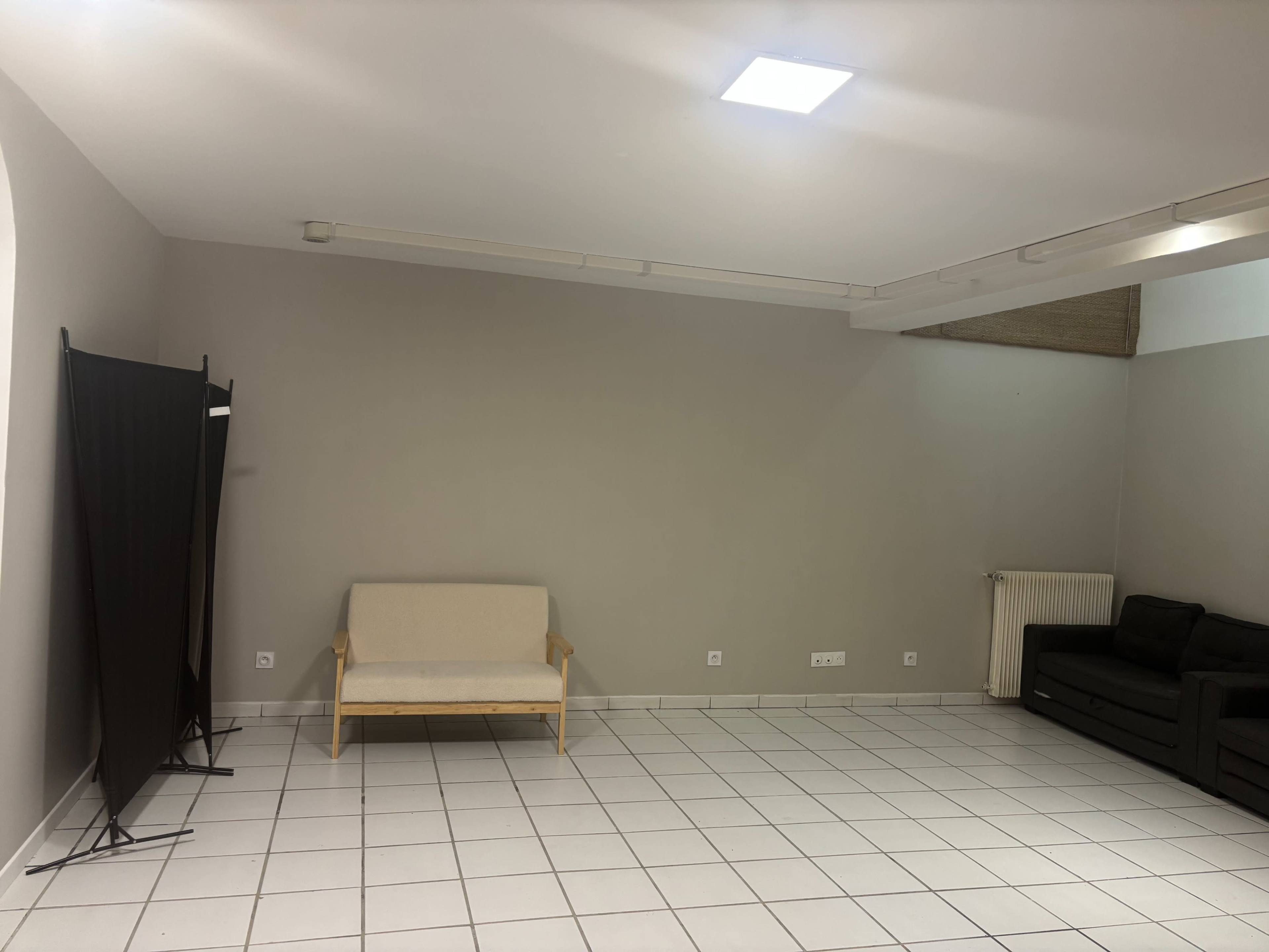 The image shows a spacious, minimally furnished room with a light-colored wall, a sofa, and two seating areas.