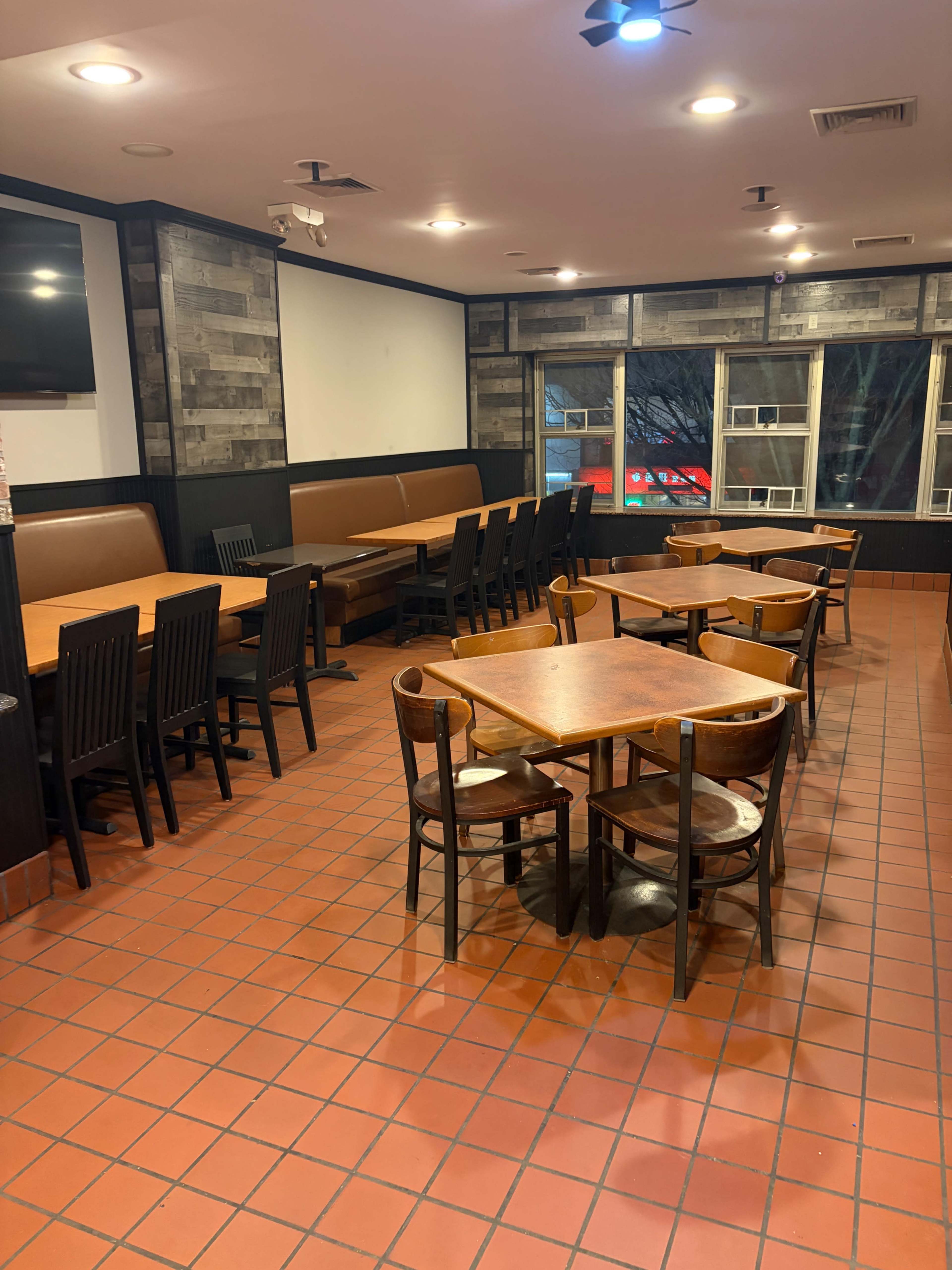 The image shows an empty restaurant interior with wooden tables and chairs arranged neatly on a tiled floor.