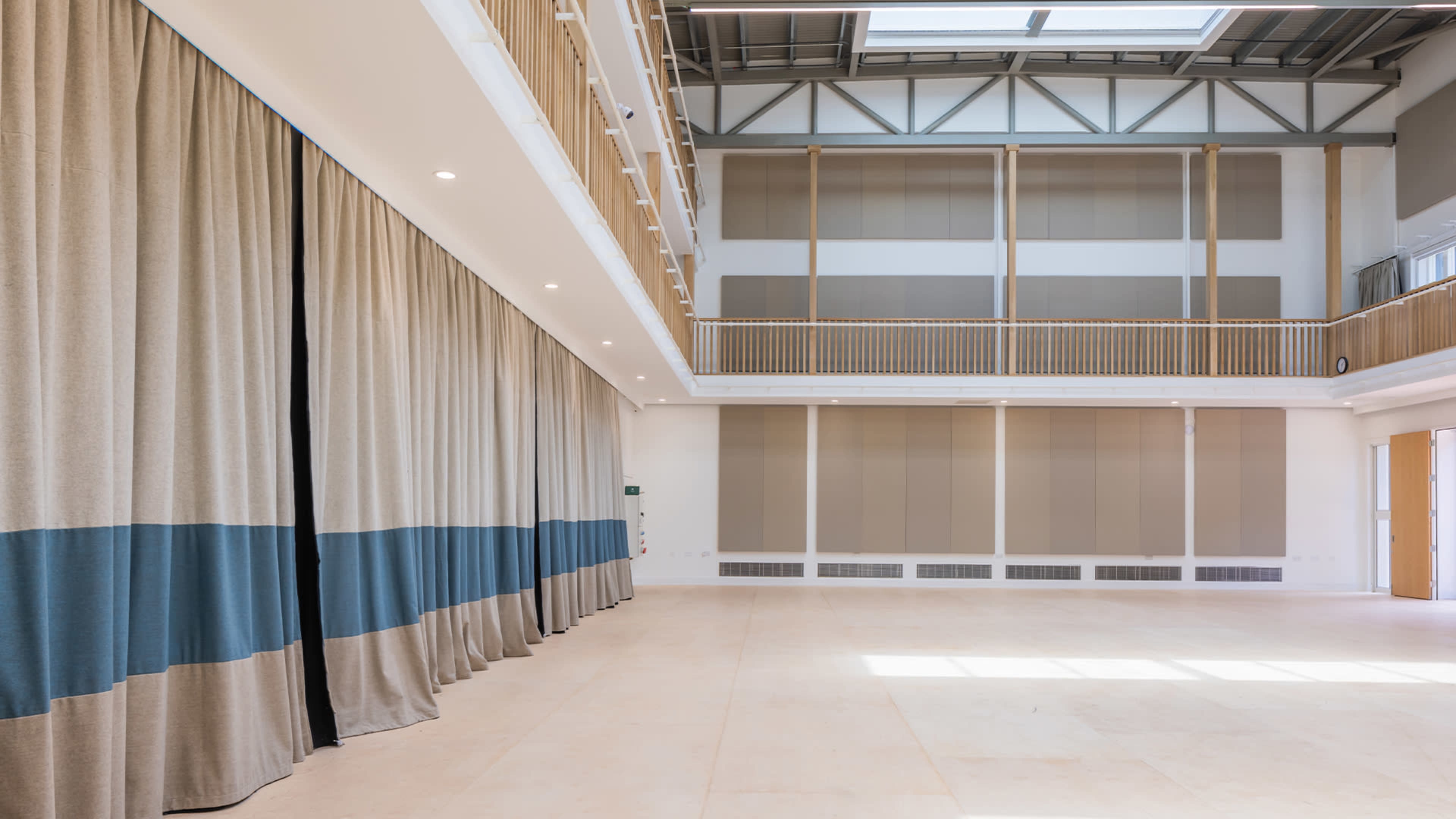 A spacious interior with high ceilings, large windows, and beige curtains featuring blue stripes along one wall.