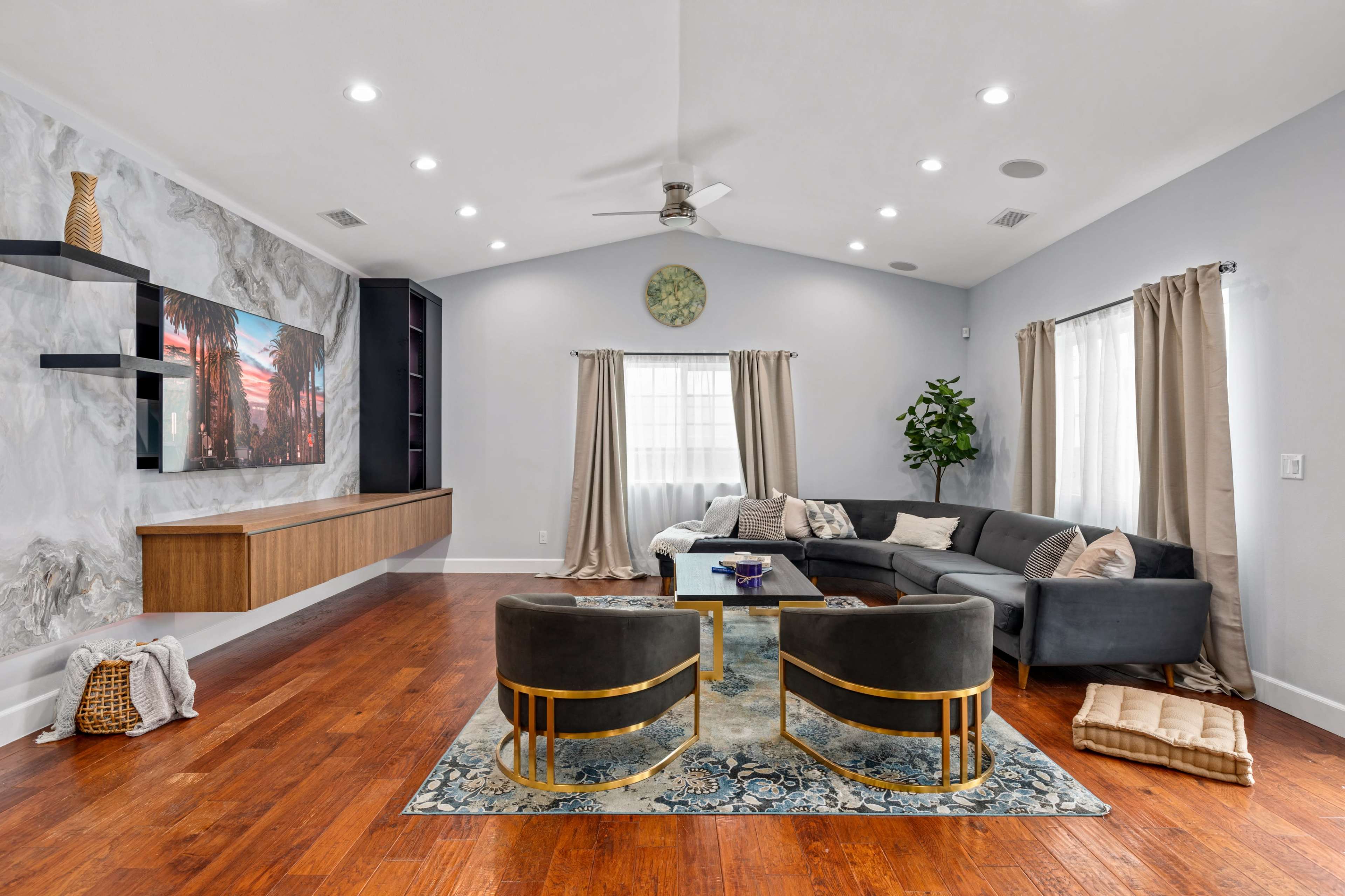 A modern living room features a sectional sofa, two armchairs, a coffee table, and a mounted television against a textured wall.