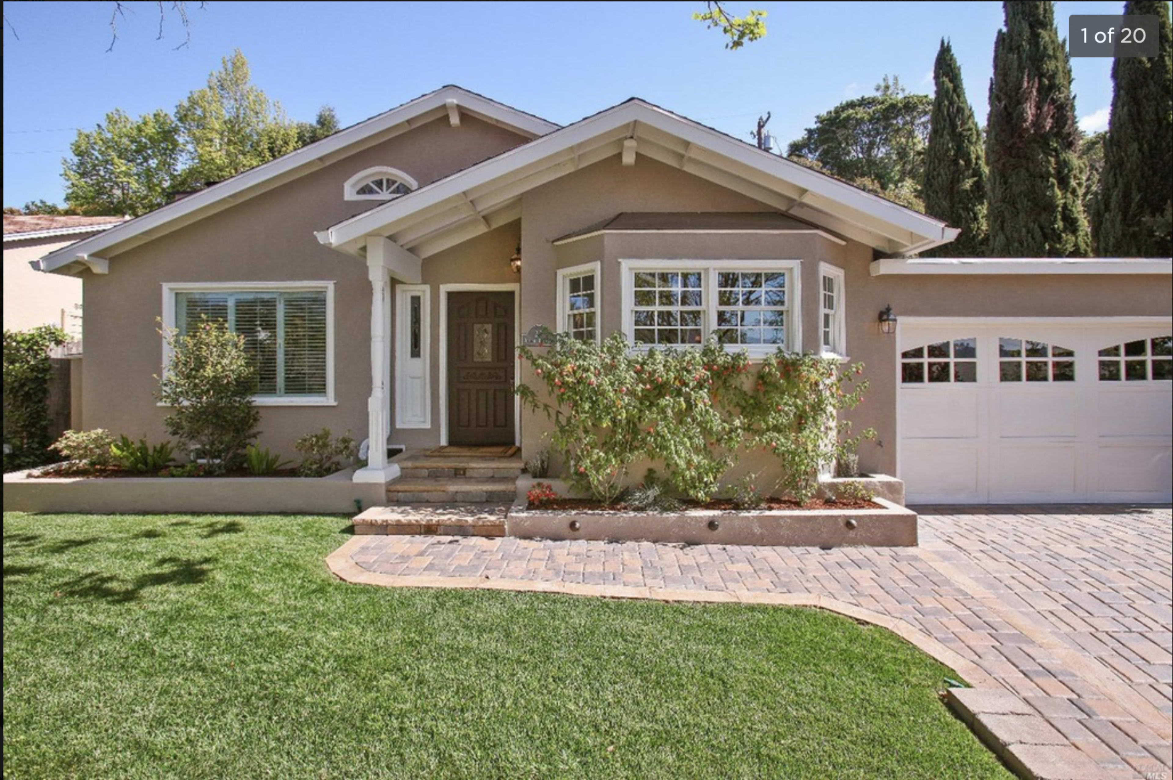 A charming single-story house with beige siding, a small front garden, and a driveway leading to a two-car garage.