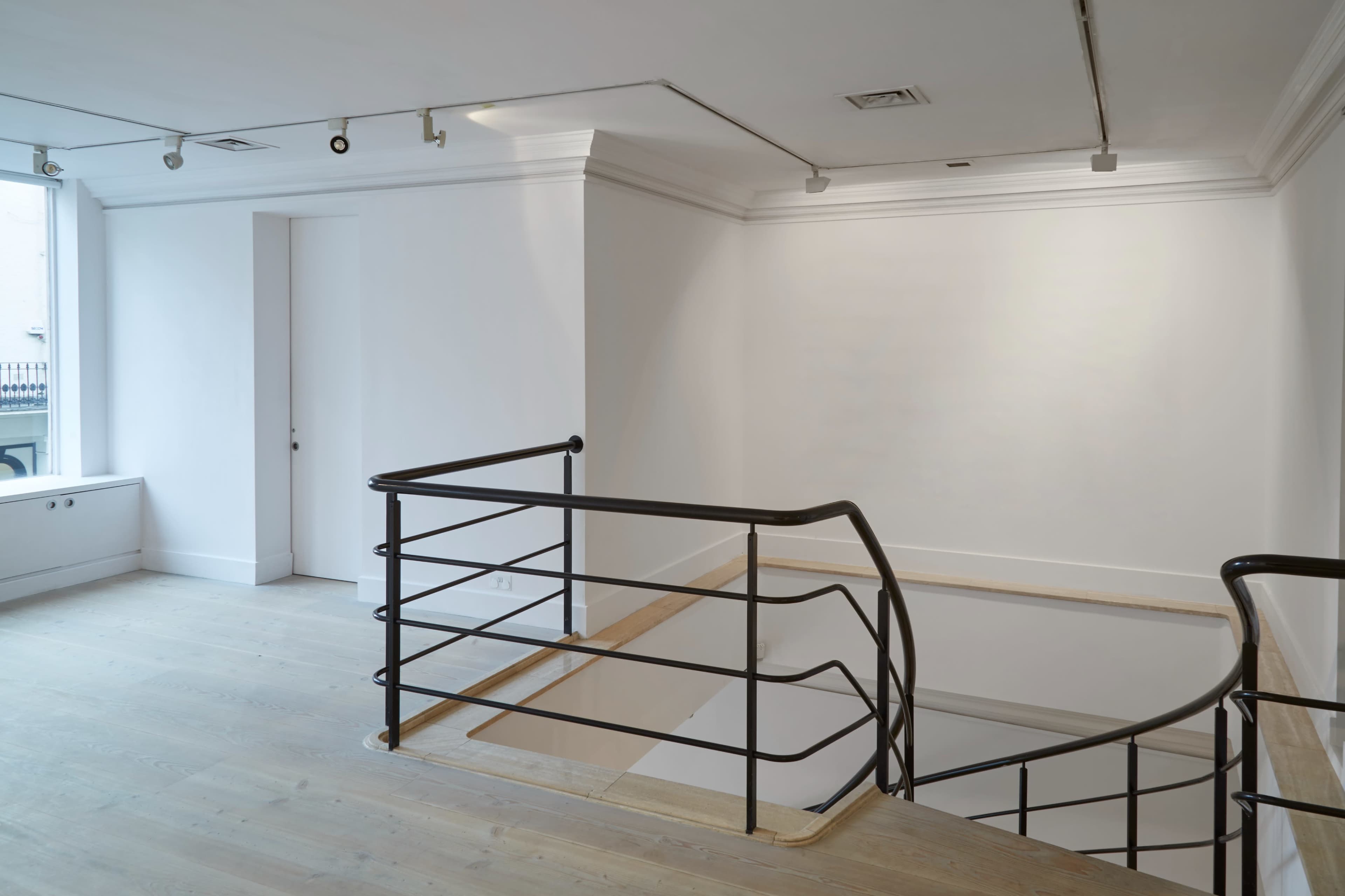 A minimalistic, empty interior space with a staircase and a railing, featuring light-colored wooden floors and white walls.