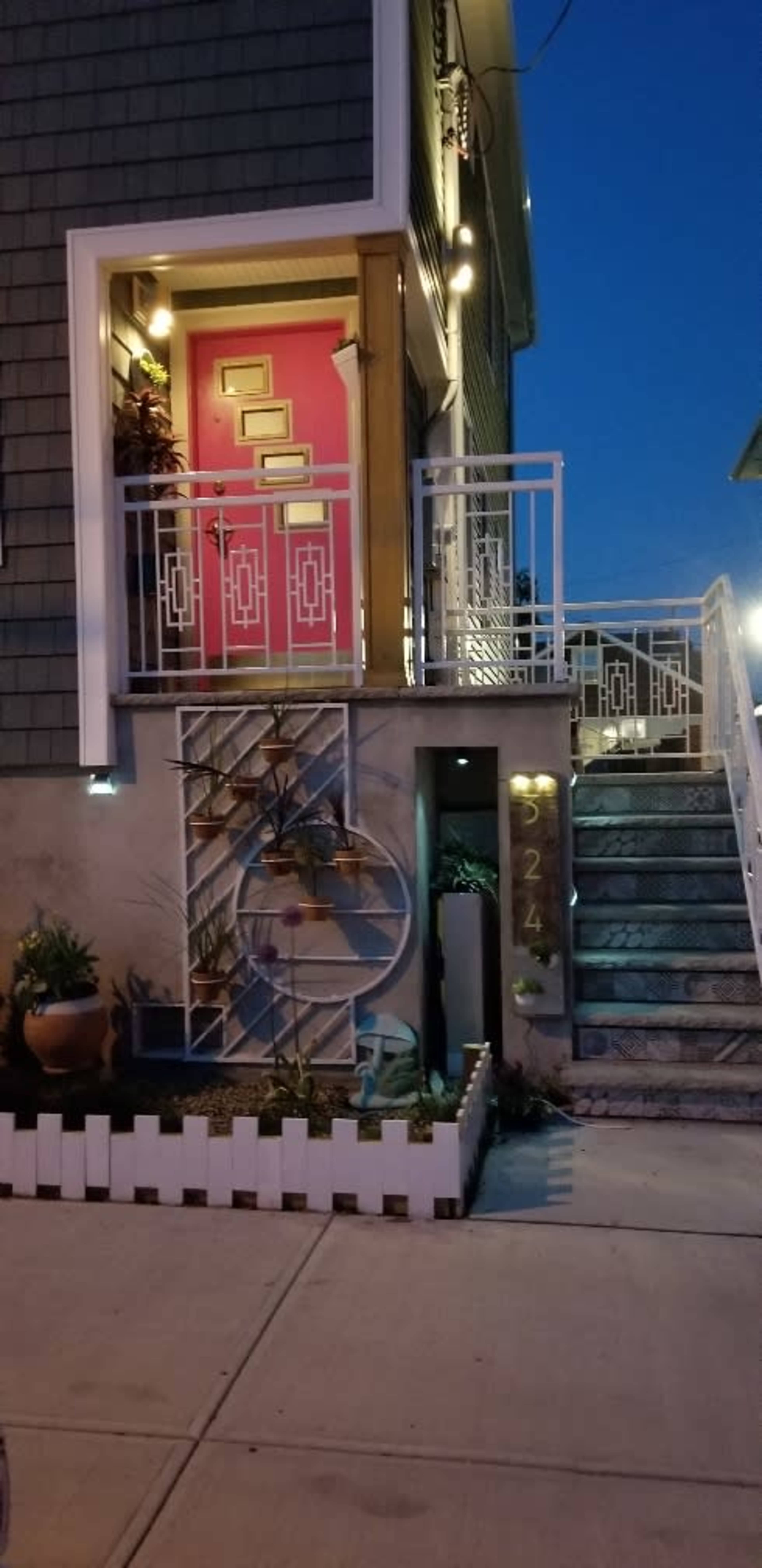 A house with a brightly colored pink front door, a decorative entrance staircase, and a small landscaped area beside the steps.