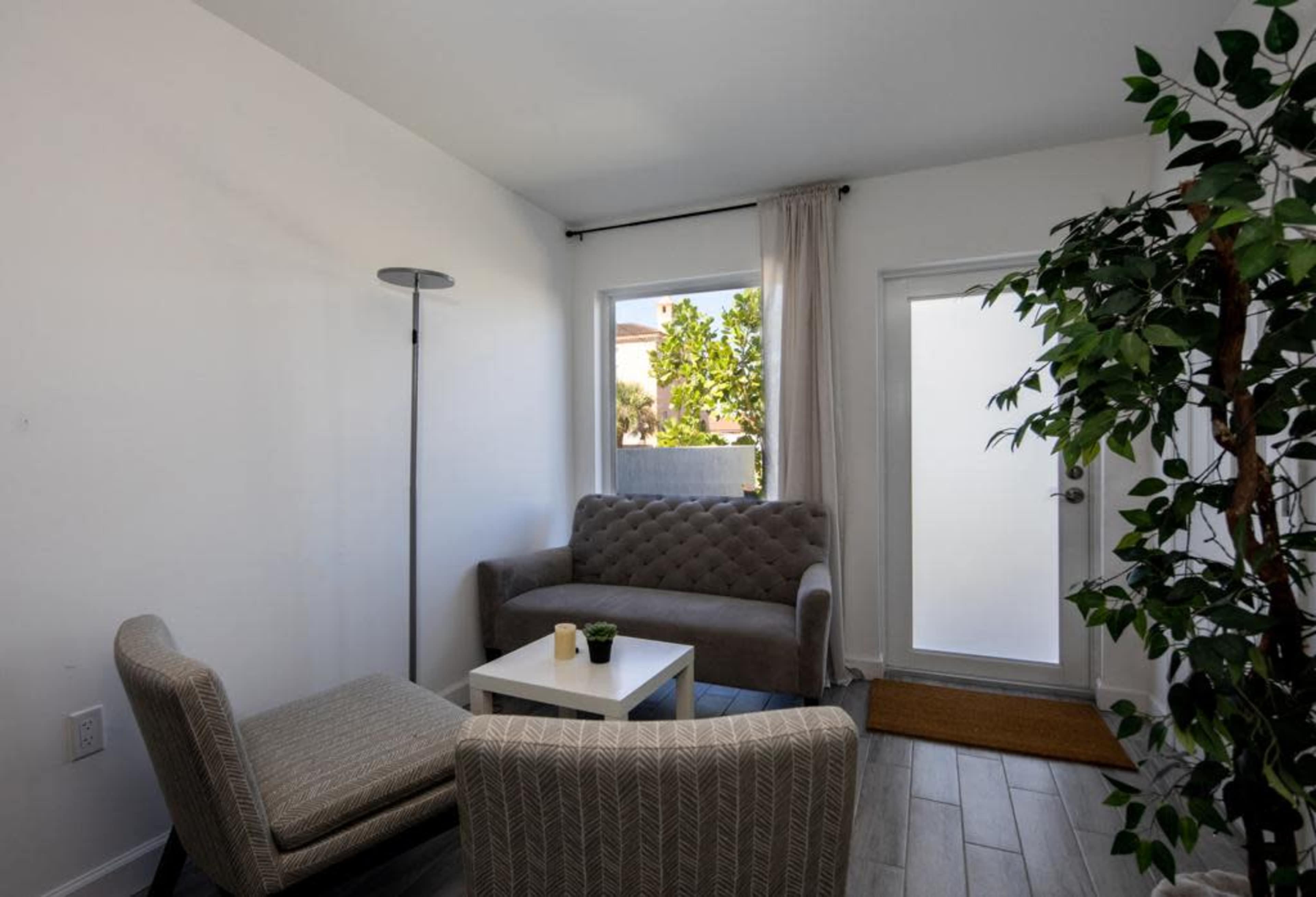 A small living area with two chairs, a gray sofa, a coffee table, and a door leading outside.