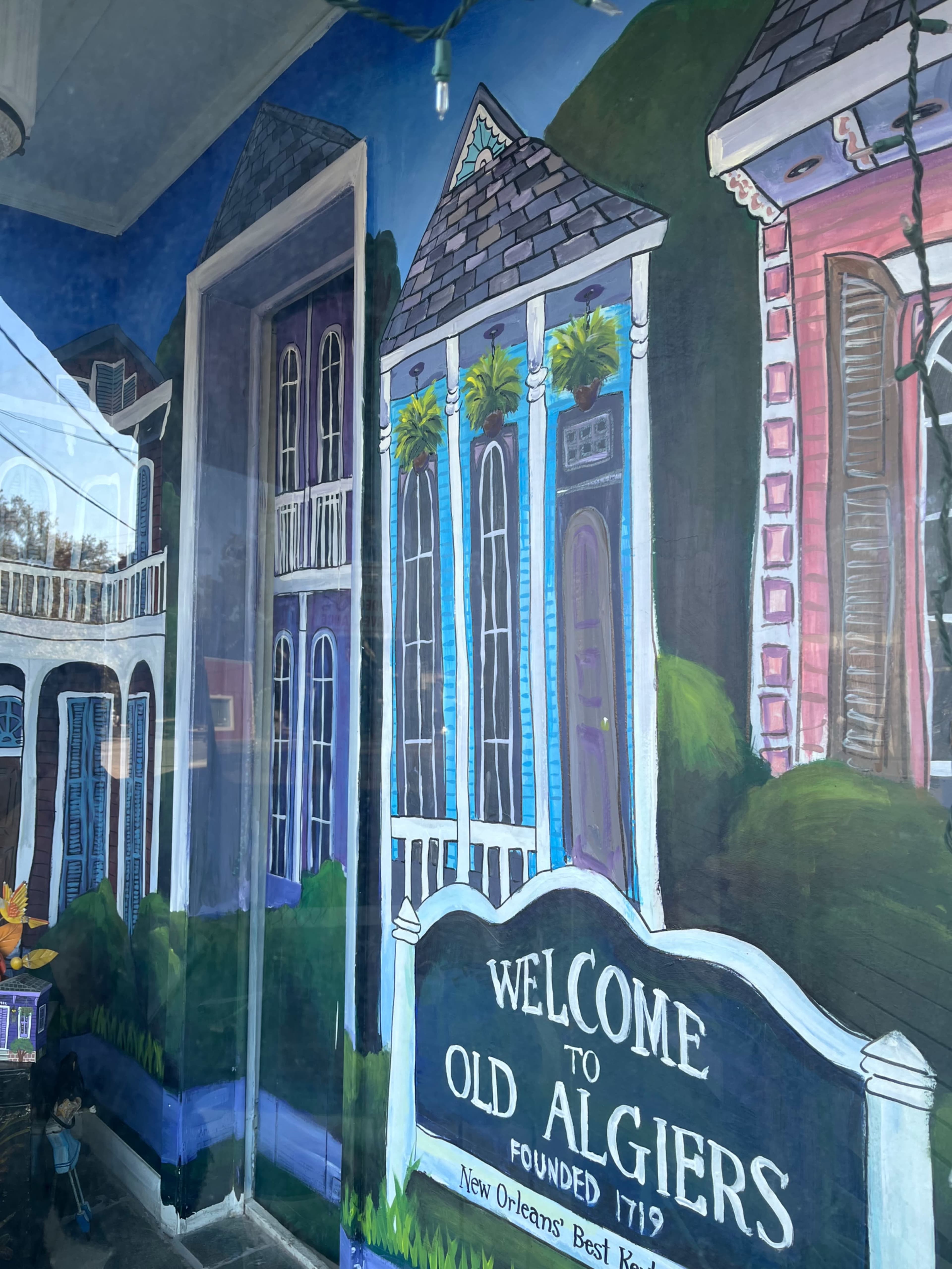 A mural depicting colorful houses in the style of Old Algiers, with a sign that welcomes visitors to the area.