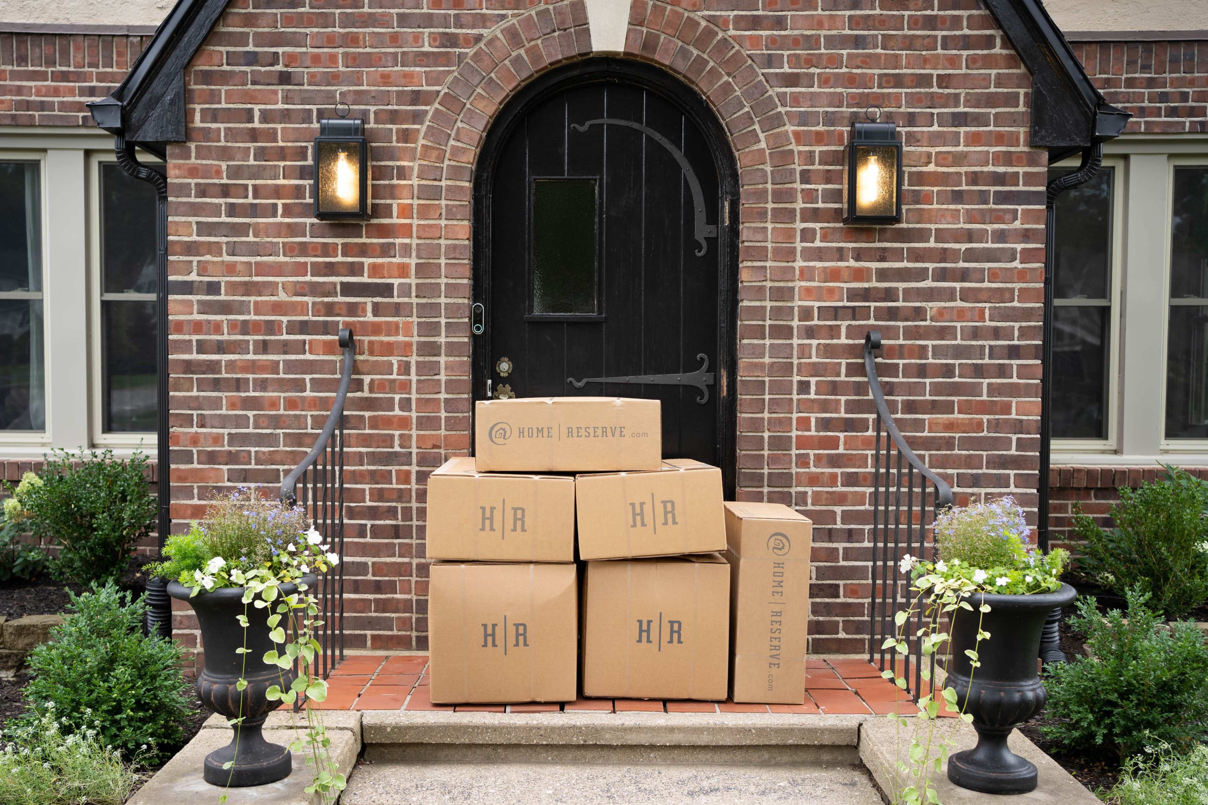 A stack of five brown cardboard boxes is placed on the front porch steps of a brick house.