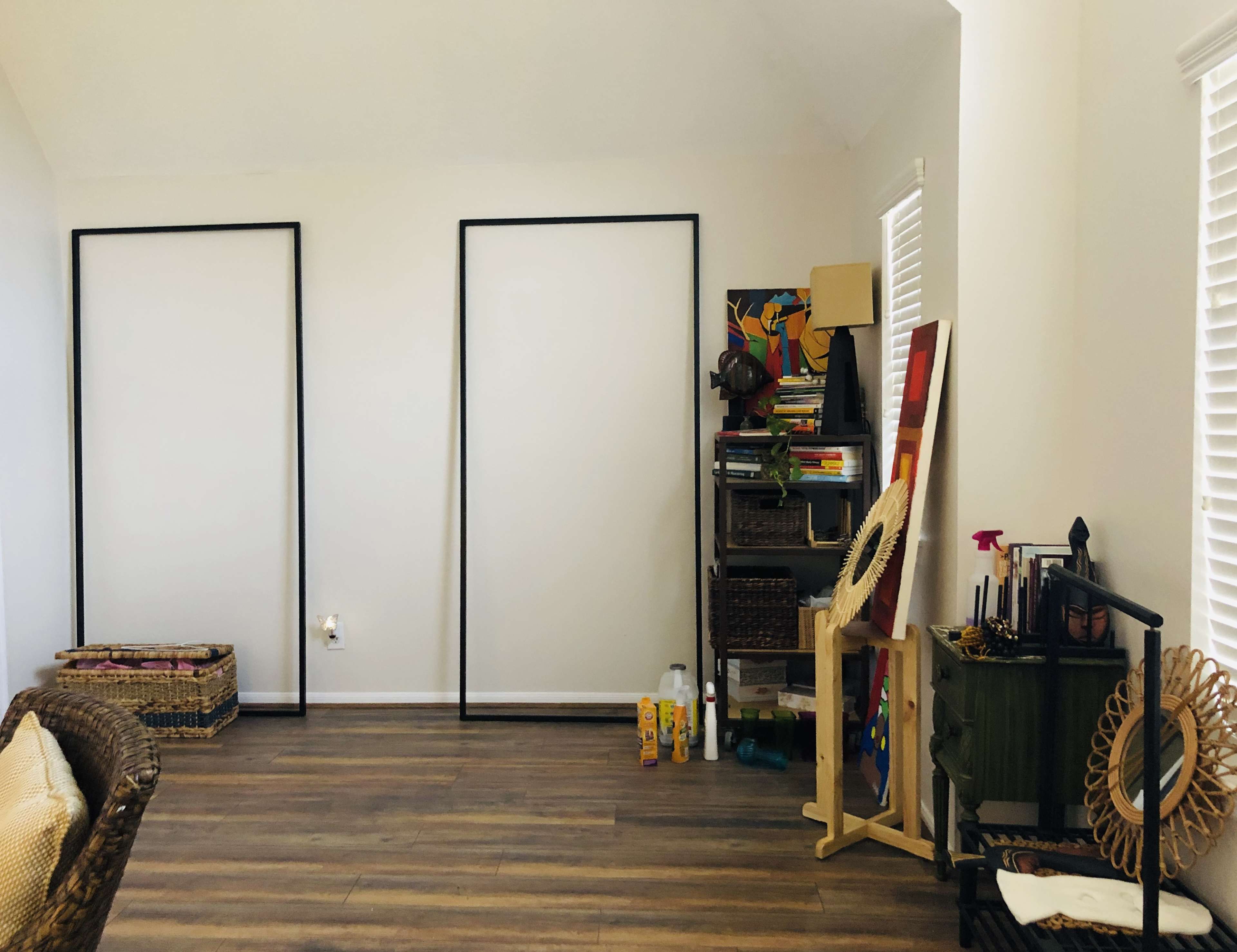 The room features two empty frames on the wall, a wicker couch, shelves with various books and items, and a wooden stand displaying crafts.
