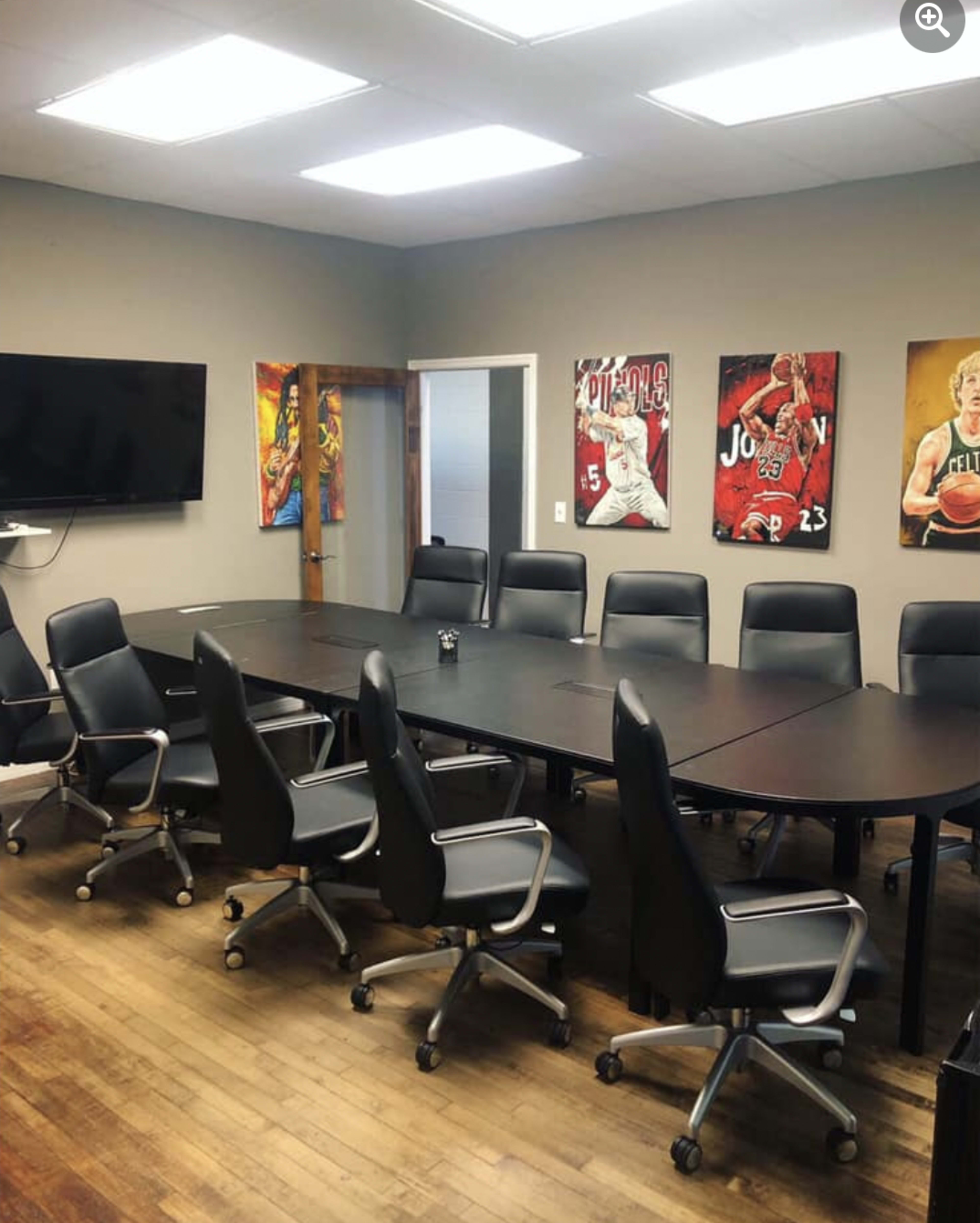 A spacious conference room with a long black table, ergonomic chairs, and sports-themed art on the walls.