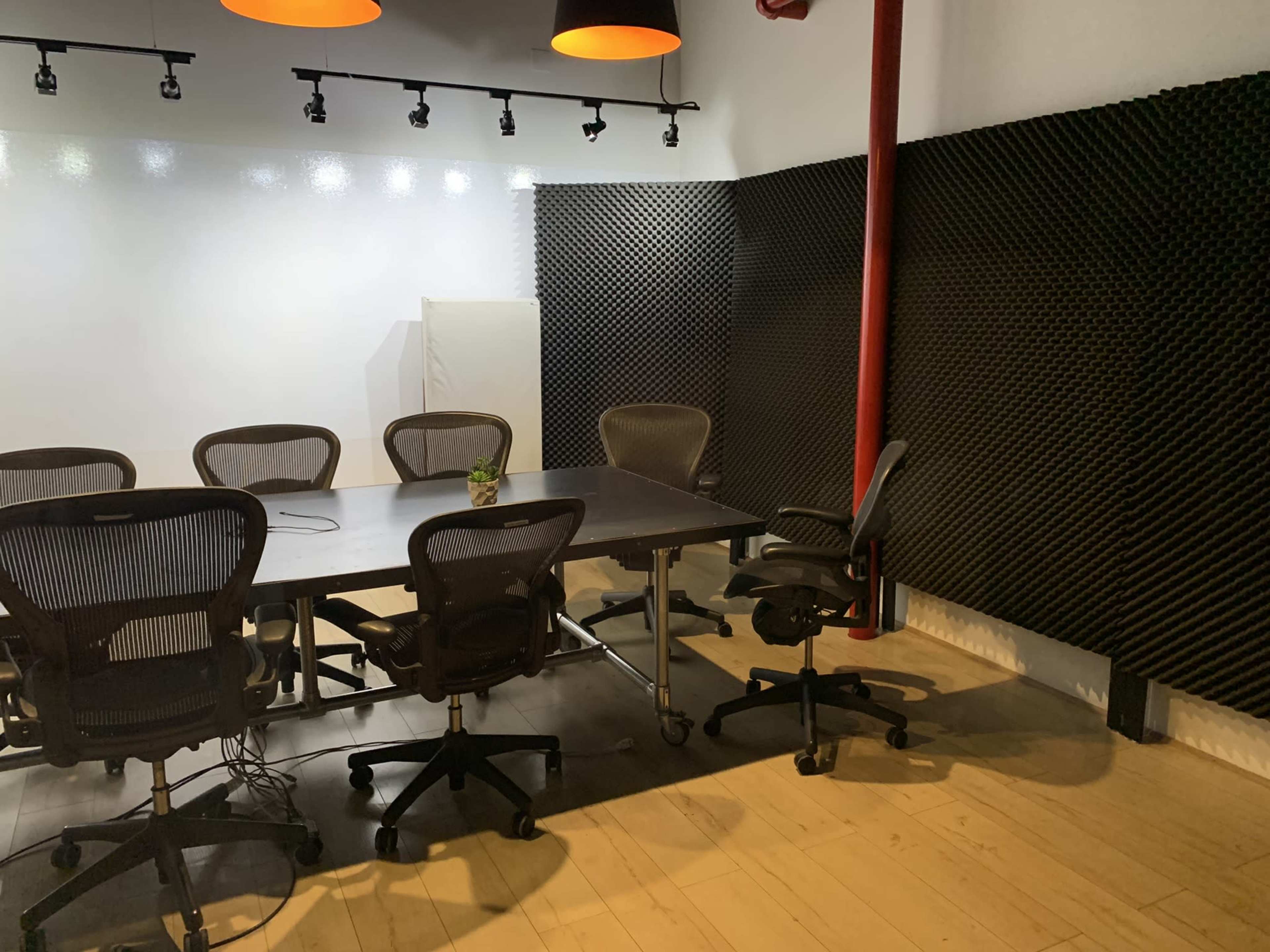 A conference room features a rectangular table surrounded by ergonomic chairs and acoustic foam panels on the walls.