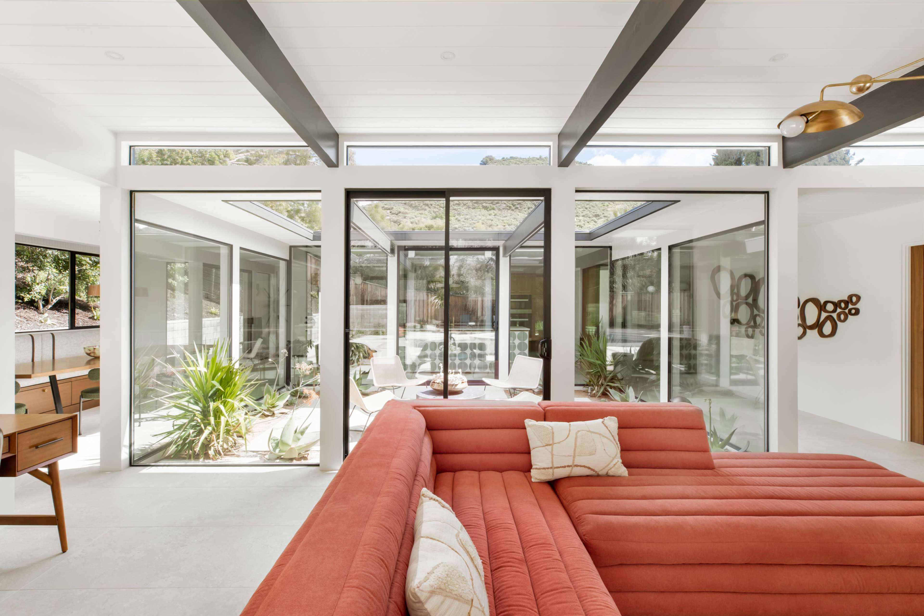 A modern, open-concept living space with a red sectional sofa and large windows overlooking a landscaped exterior.