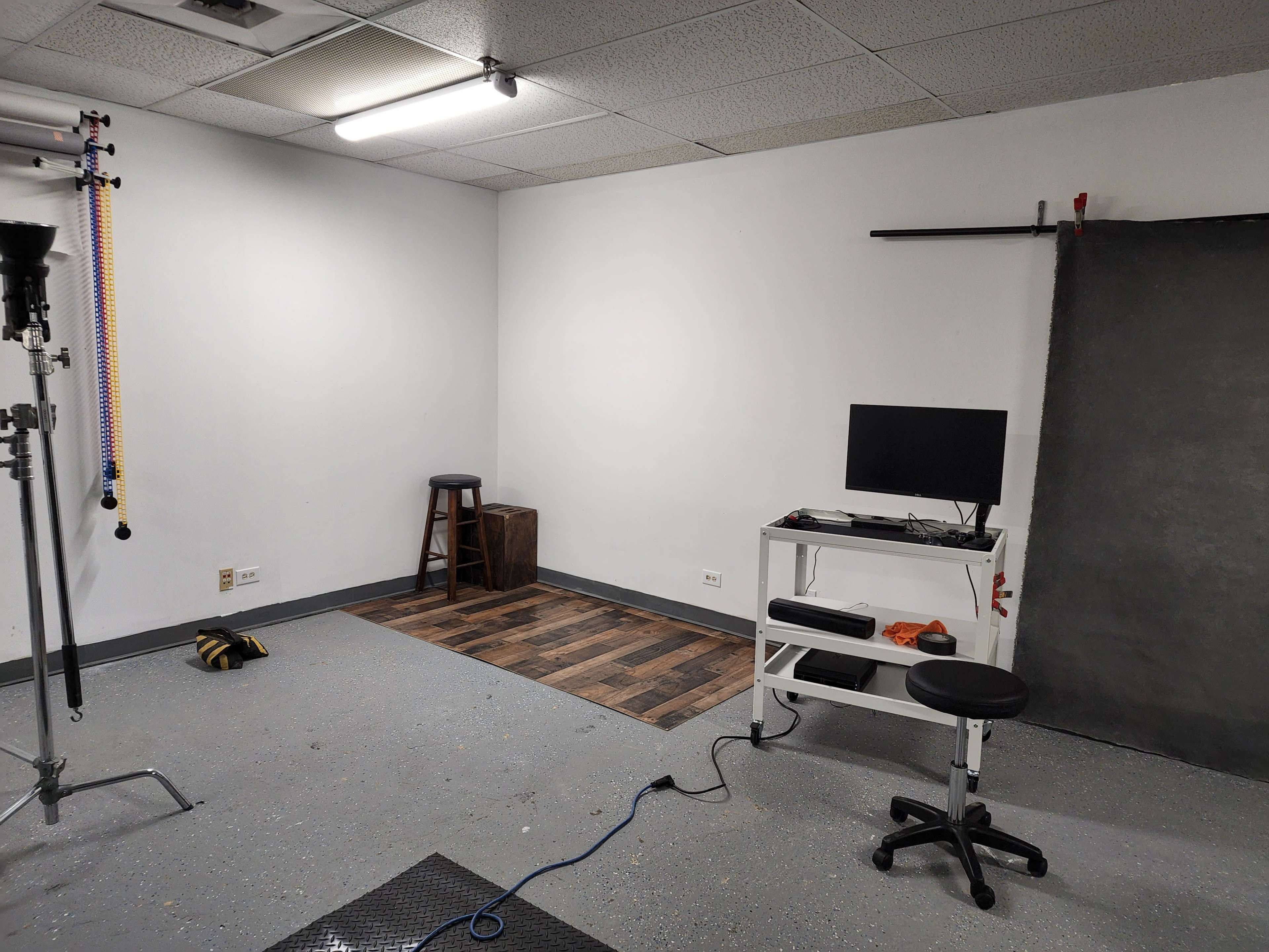 A minimalist studio environment with a monitor on a mobile workstation, a stool, a wooden box, and a backdrop setup.