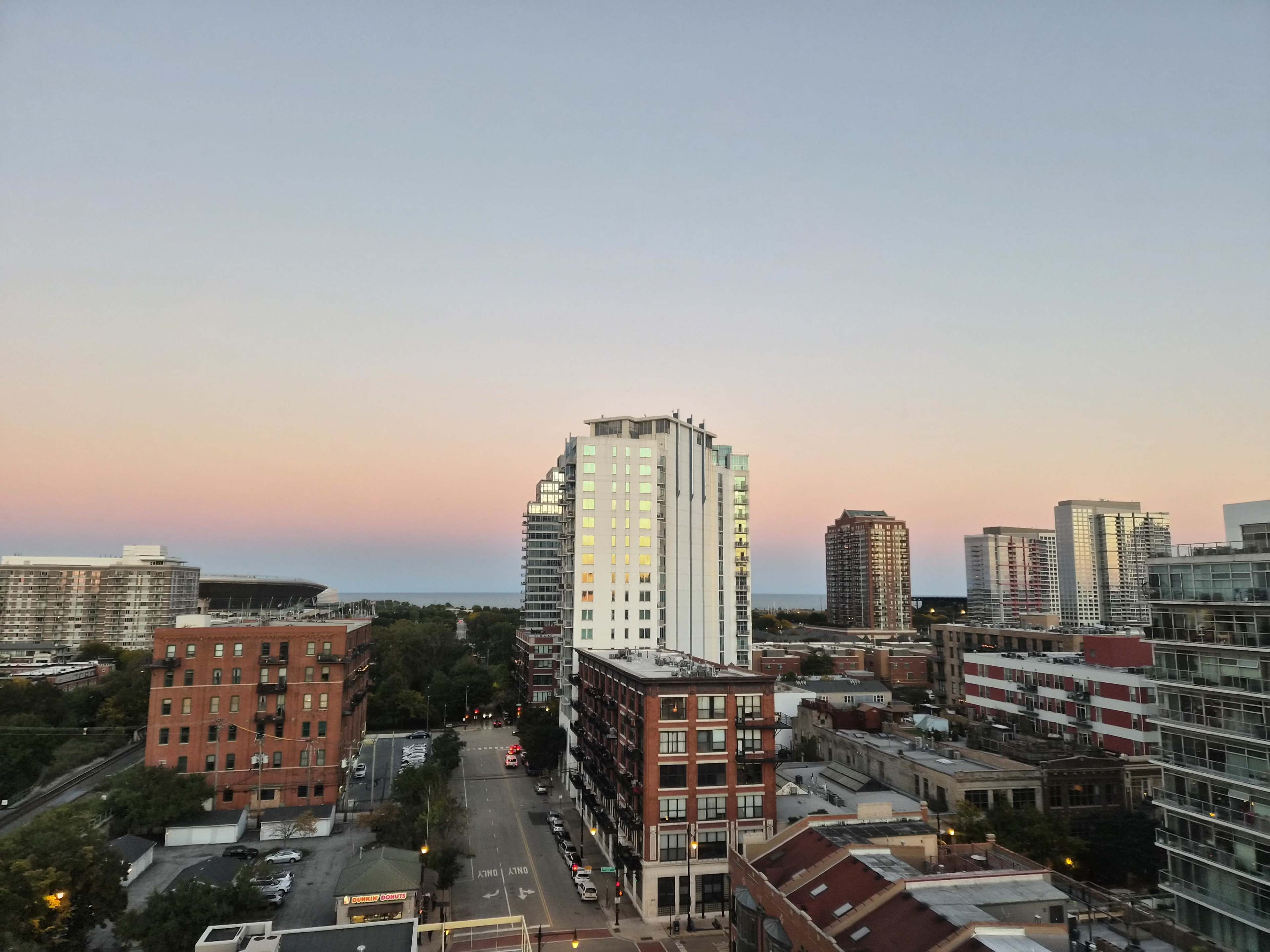 The image shows a city skyline at dusk, with buildings of various heights and a lake visible in the background under a gradient sky.