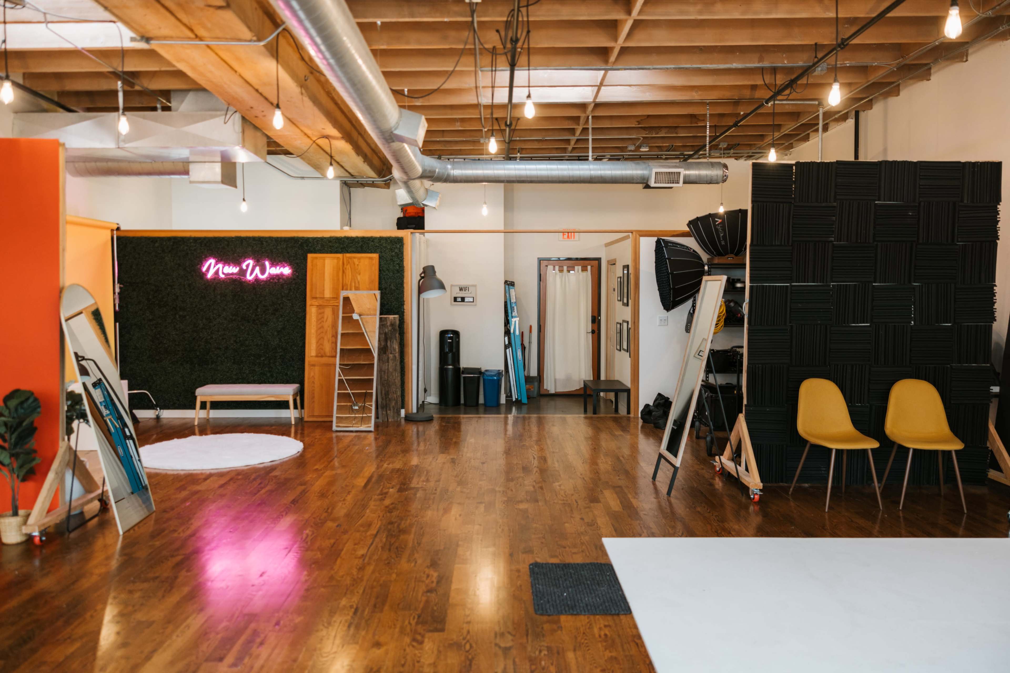 An interior space features wooden flooring, exposed beams, a neon sign that reads "New Wave," and various props and furniture, including chairs and shelving units.