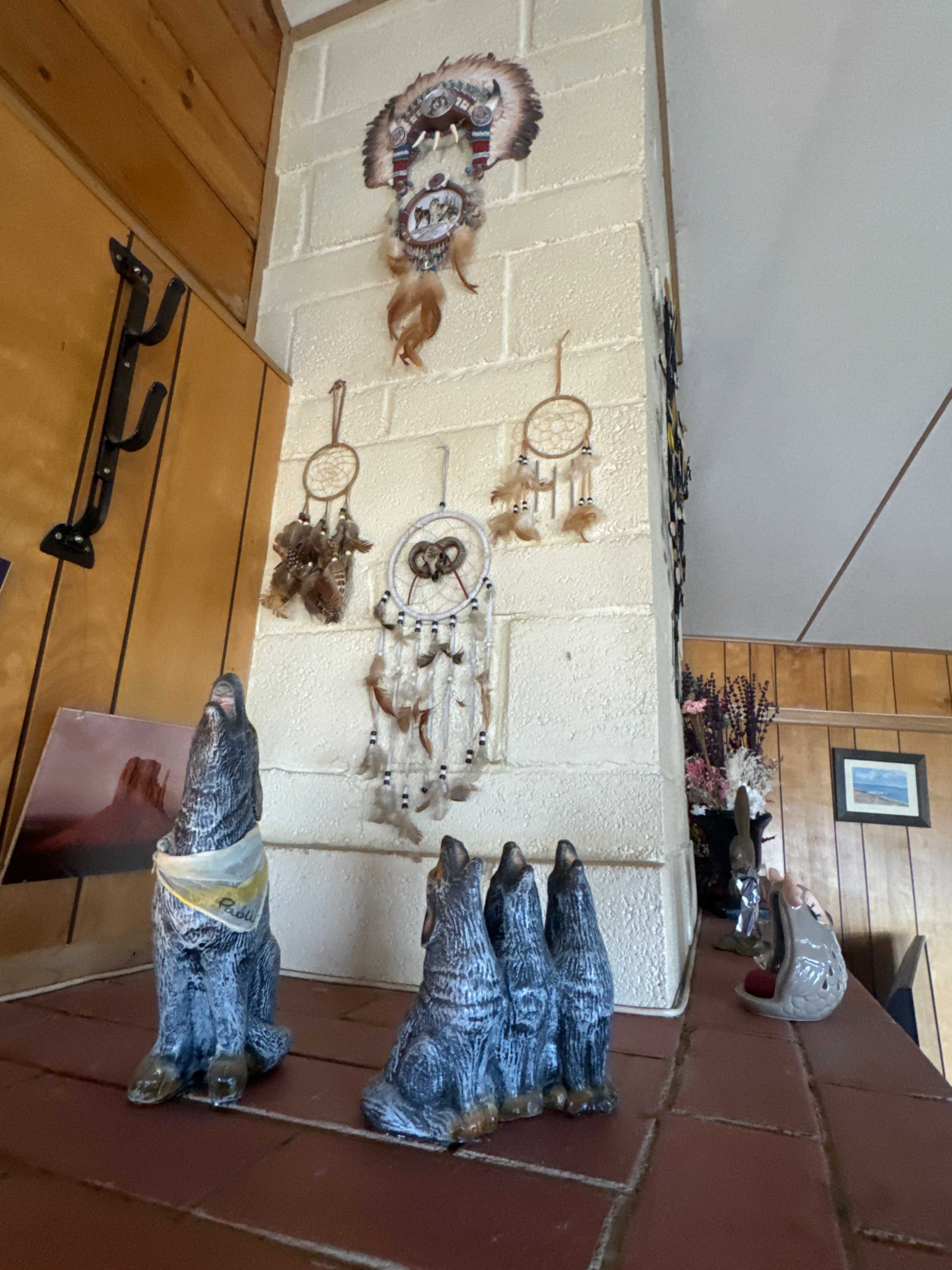 The image shows a brick fireplace with decorative items, including three wolf sculptures and a dreamcatcher hanging on the wall above.