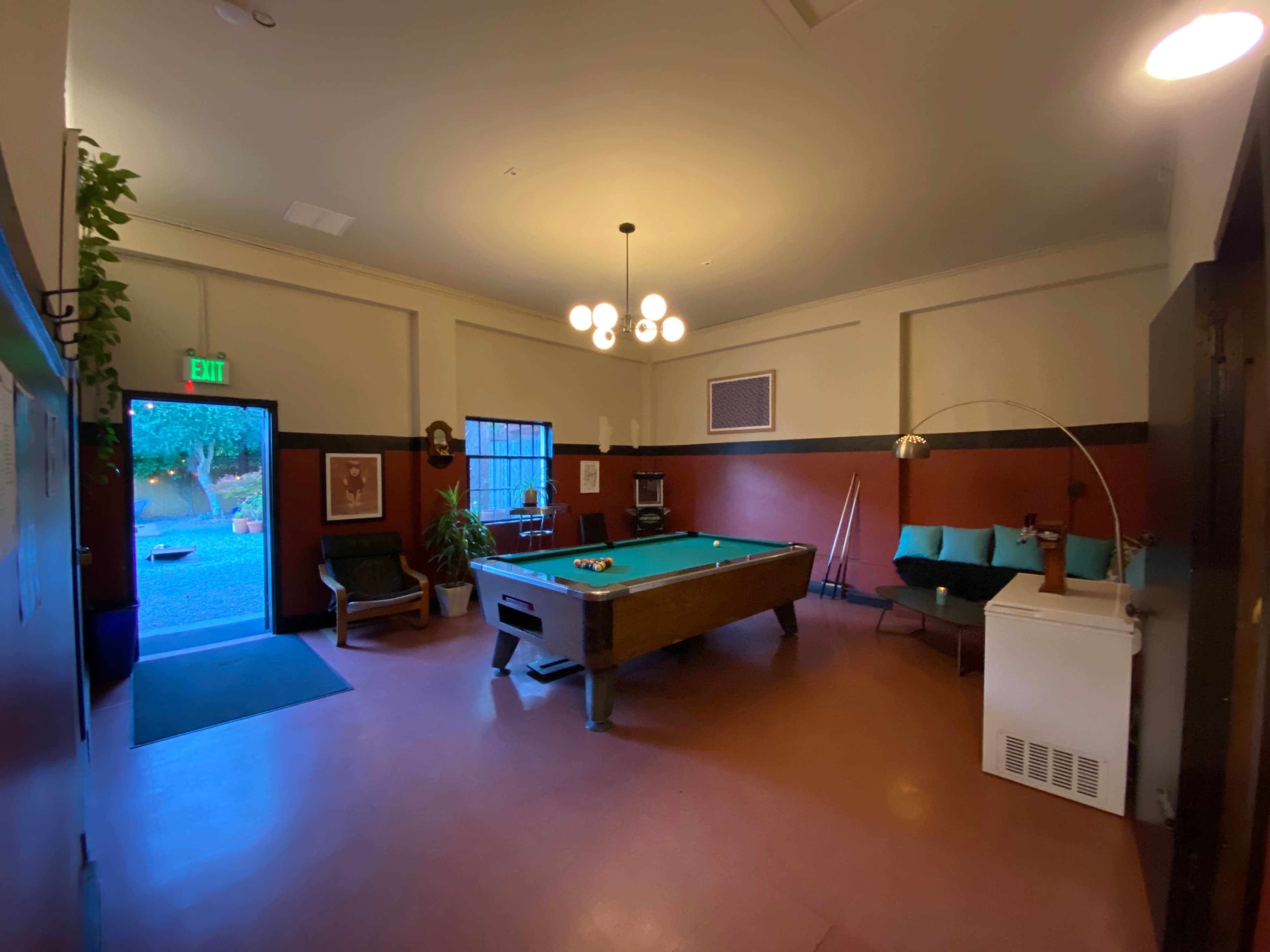 A room with a pool table, a lounge chair, and a door leading to an outdoor area.