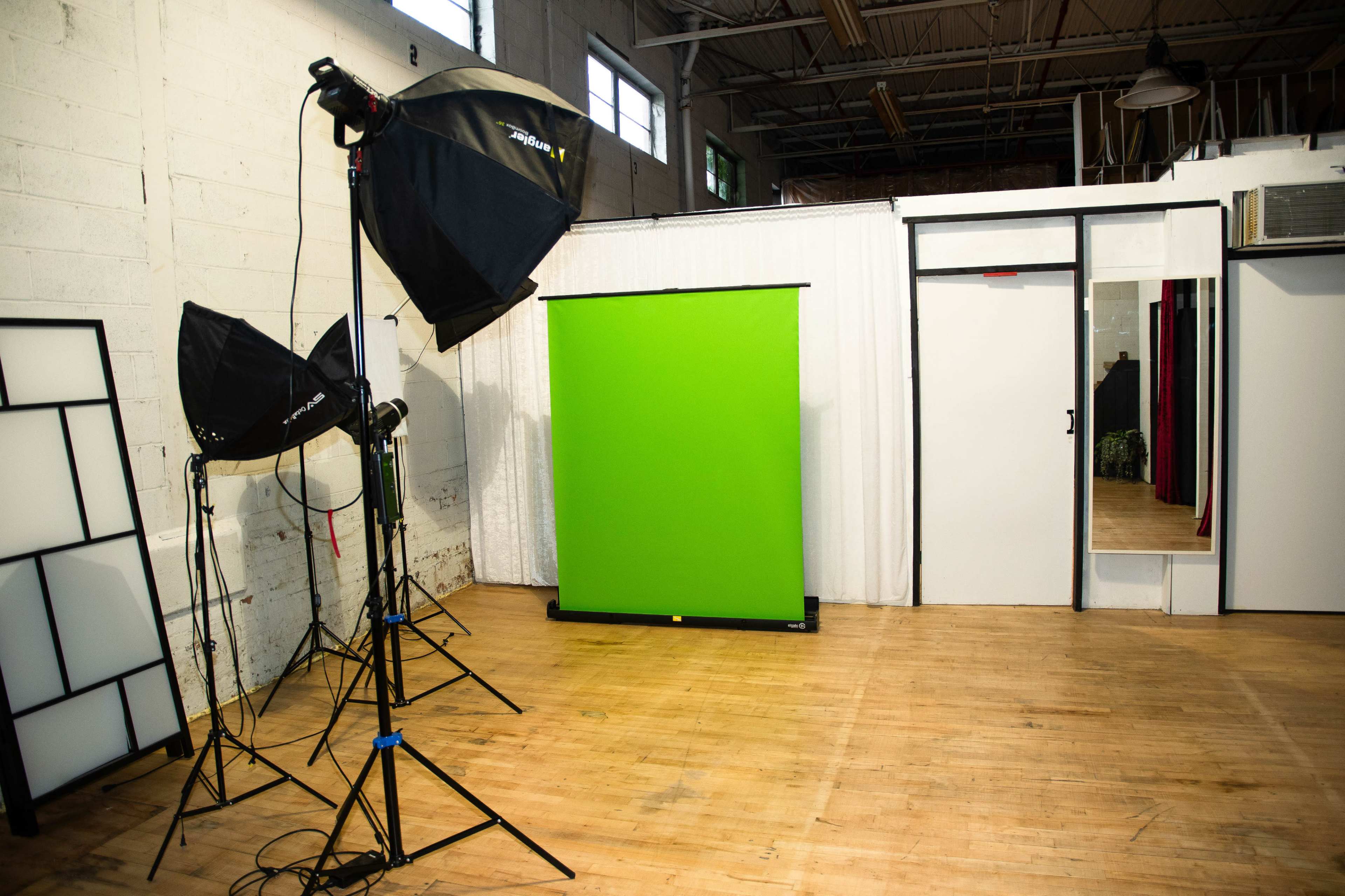 The image shows a photography studio with a green backdrop, softbox lights, and a doorway leading to another room.