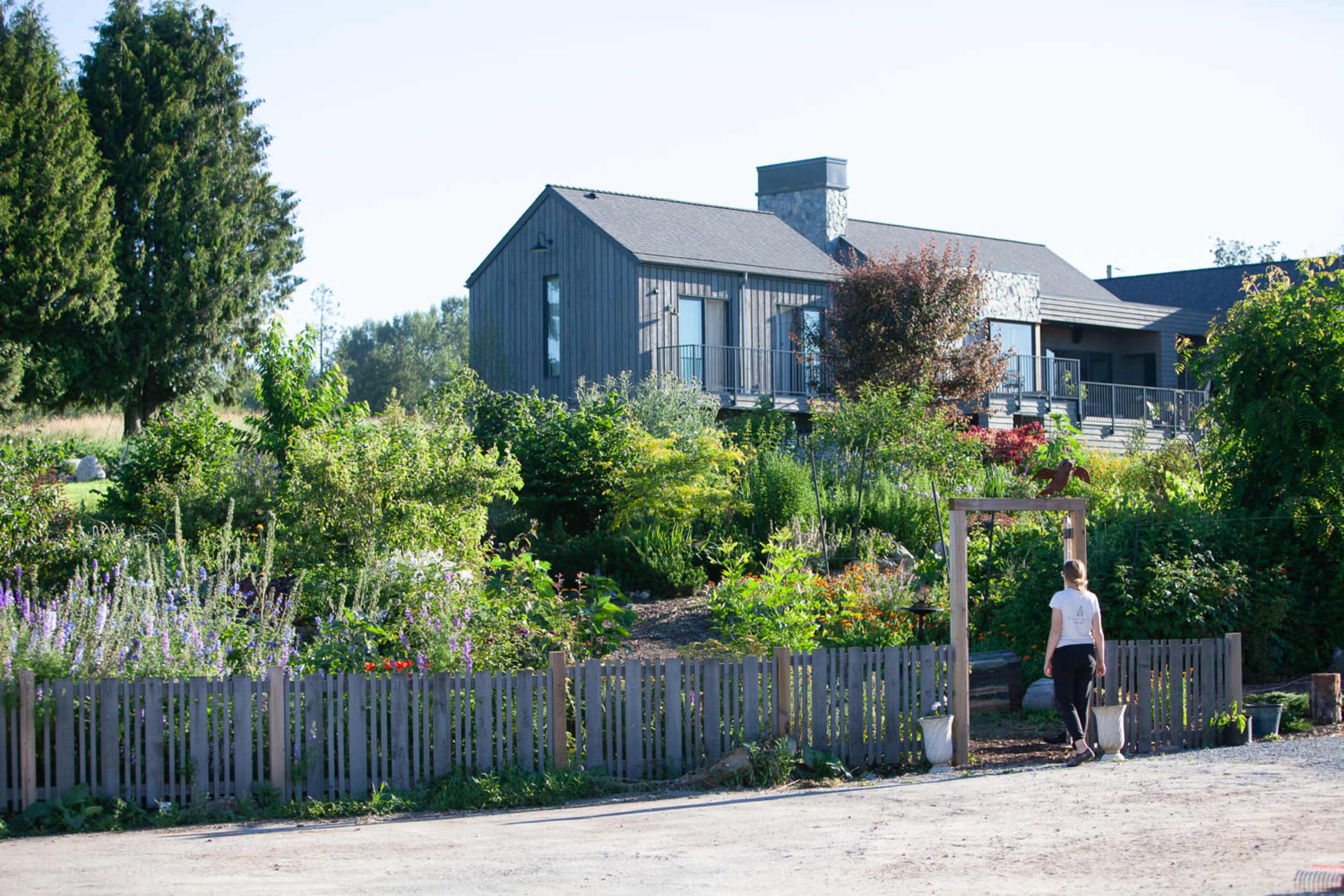 A woman walks through a garden in front of a modern house surrounded by greenery.