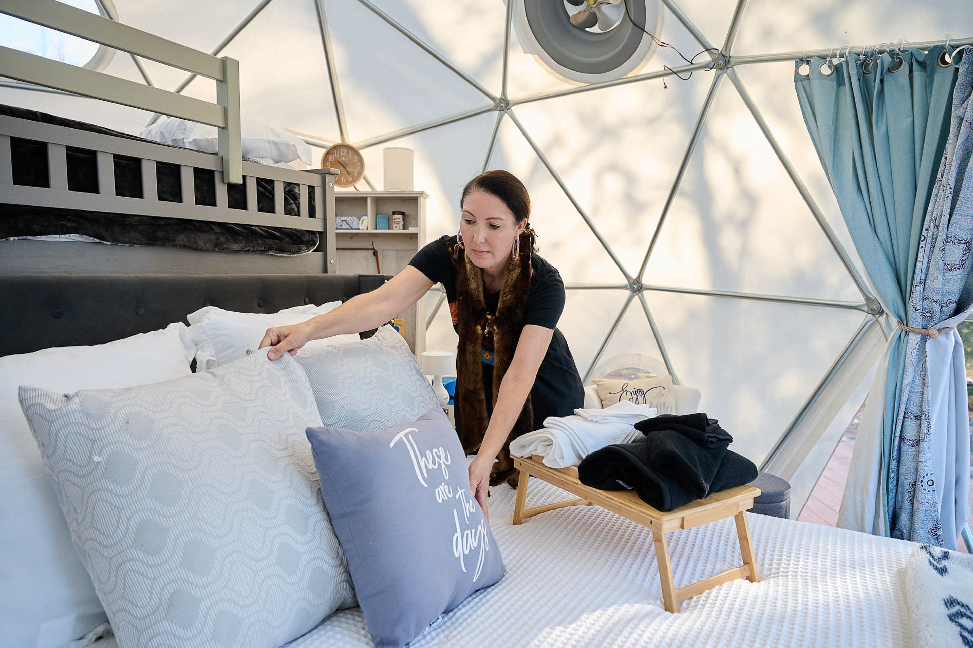 A woman arranges pillows on a bed inside a geodesic dome.