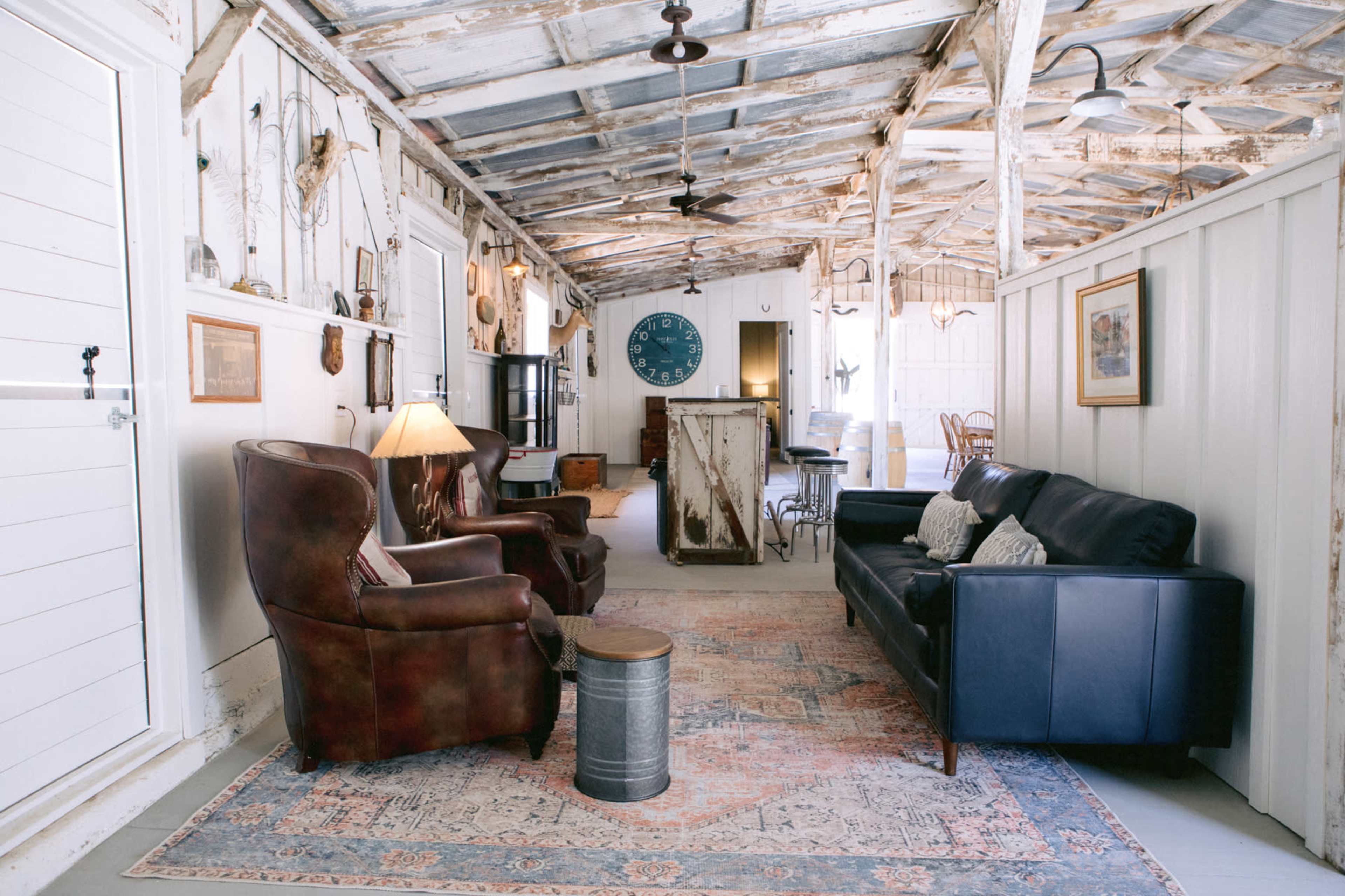 A rustic interior of a room with two armchairs, a sofa, and a coffee table, set against a backdrop of wooden beams and vintage decor.