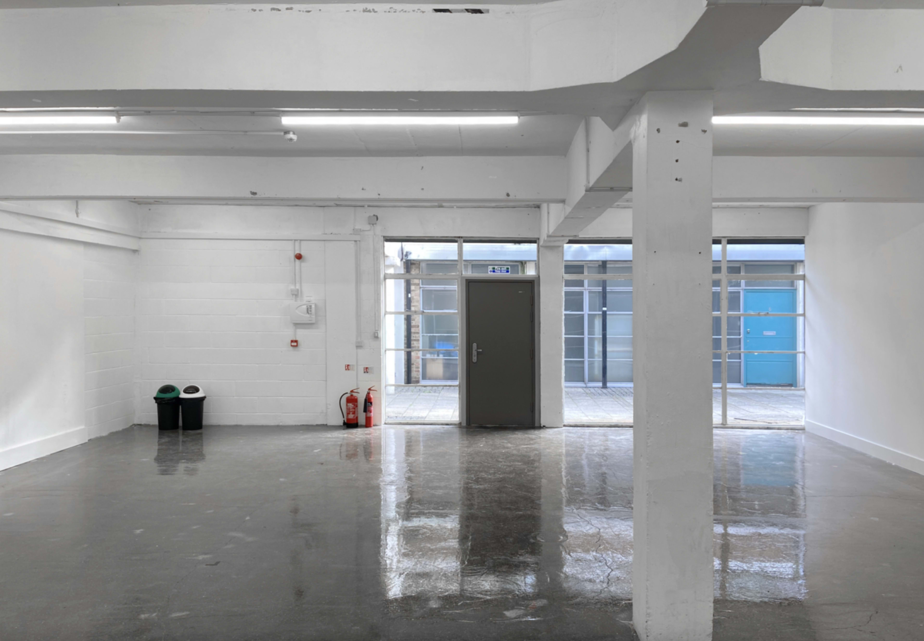 A large, empty, well-lit room with polished concrete floors and a door leading to an outdoor area.