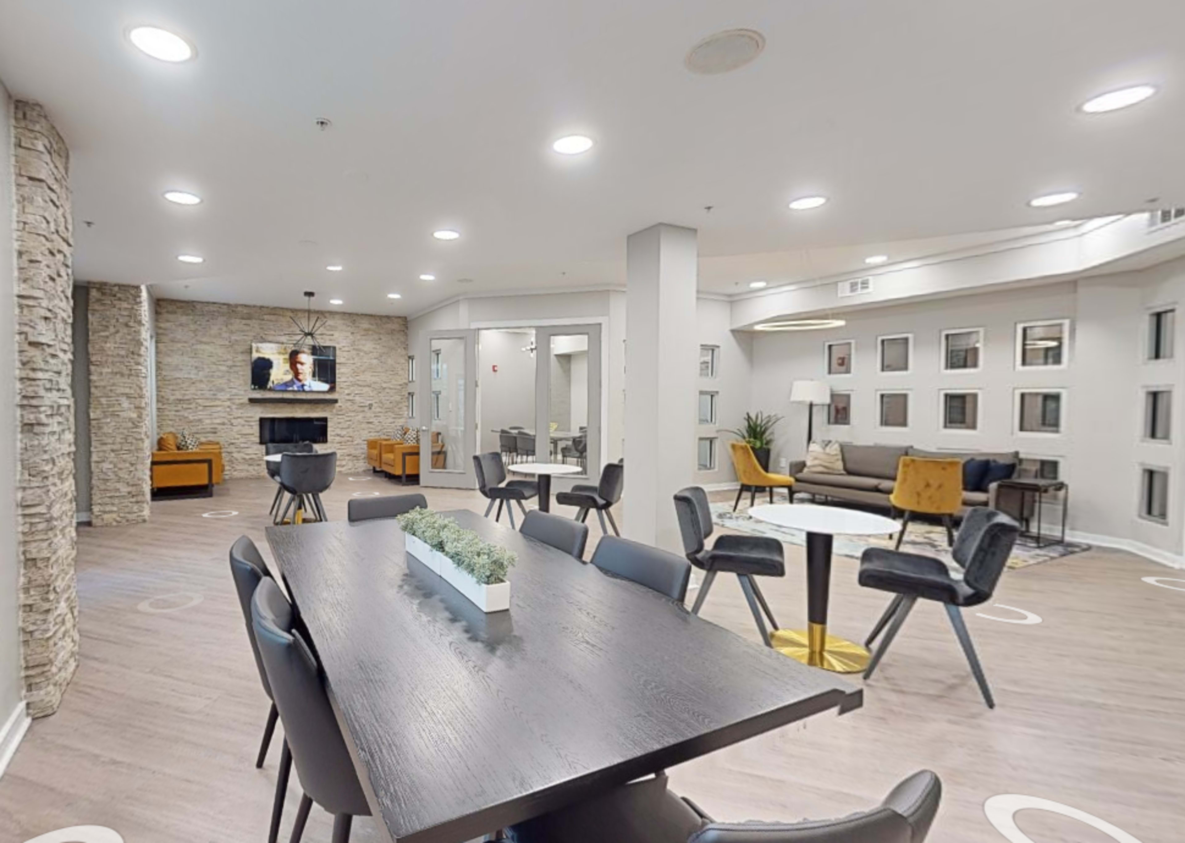 A modern, open communal area with a dining table, seating arrangements, and a television on the wall.