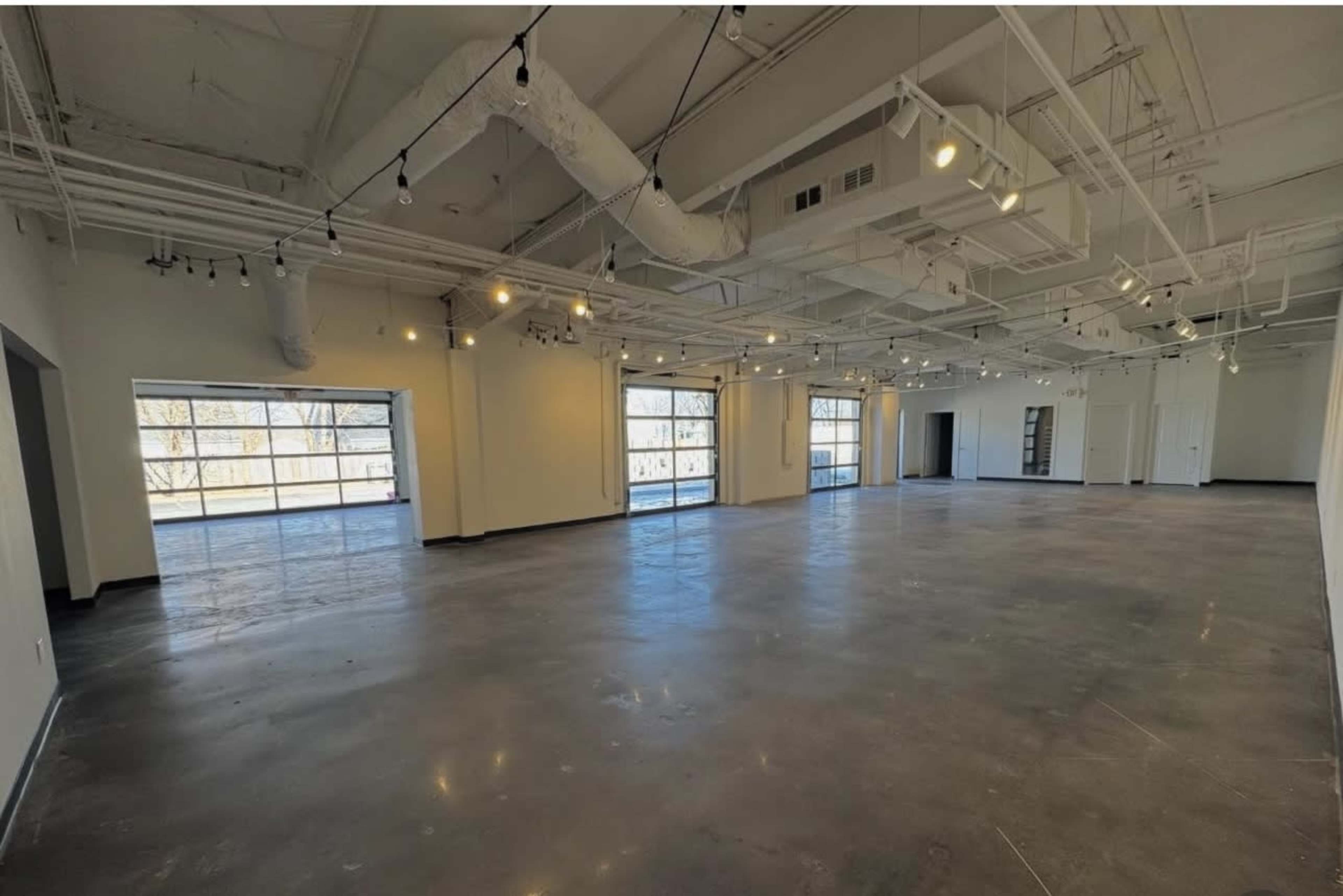 The image shows a spacious, empty commercial interior with large windows and overhead lighting.
