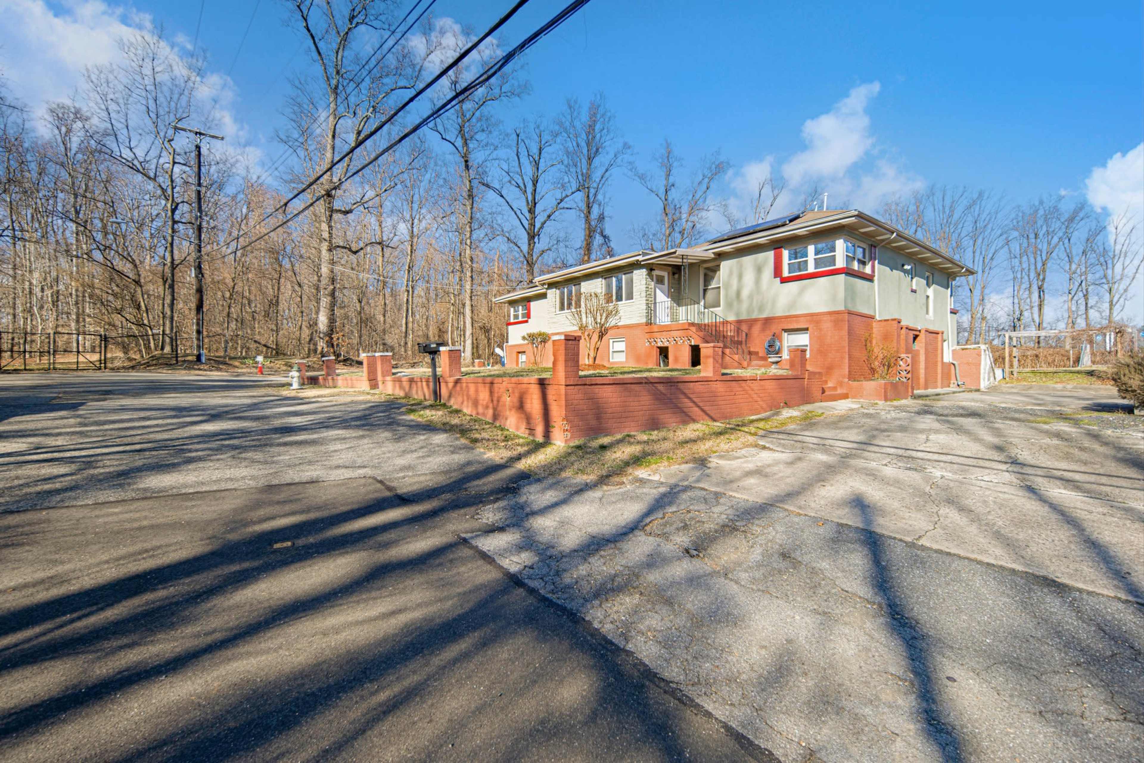 A two-story house sits at the intersection of two roads, surrounded by bare trees on a clear day.