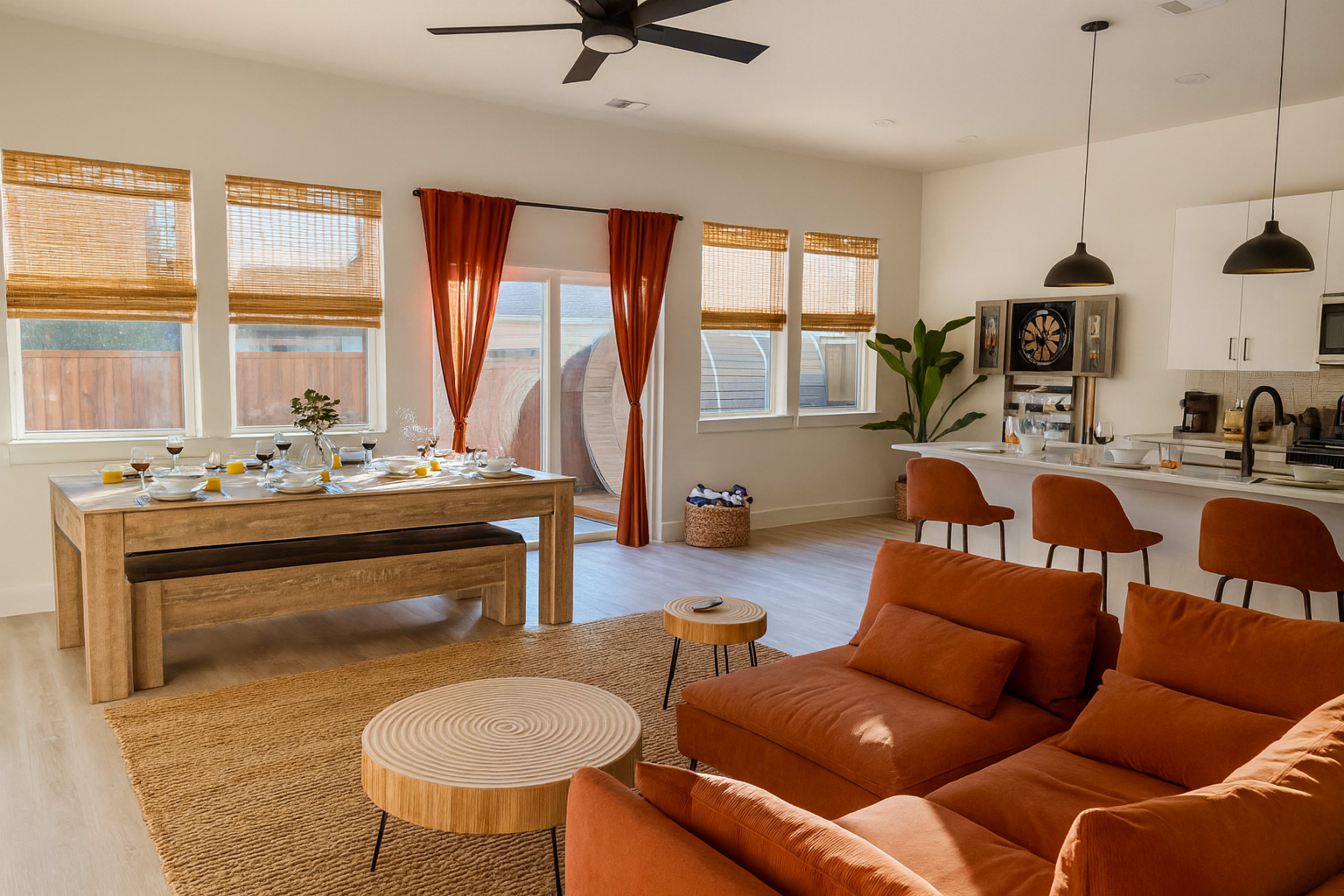 The image shows a stylish, modern living space featuring a dining table set for breakfast, a cozy seating area with an orange sofa, and a kitchen with bar stools.